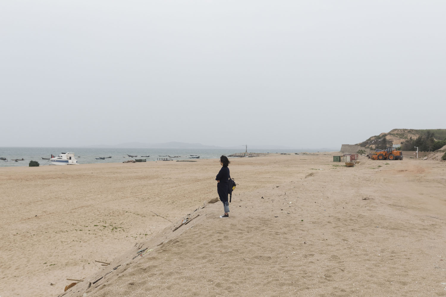 A woman standing at the top of a dune, overlooking Guanyinshan Fantasy Beach. Xiamen, China. 2018.