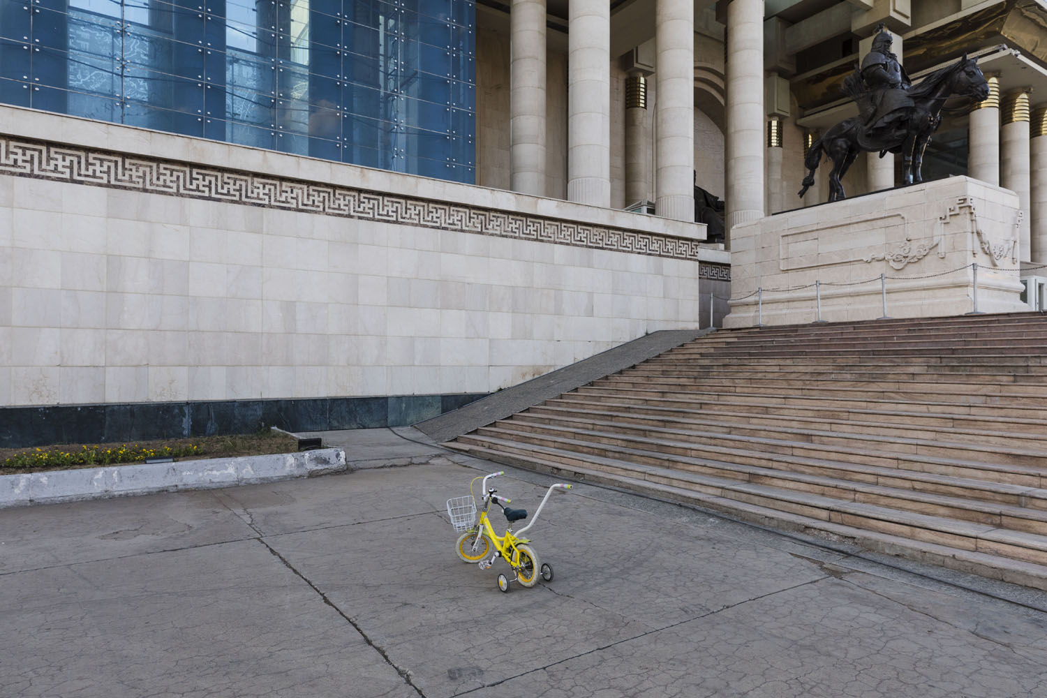 A toddler's tricycle in front of the parliament building in Genghis Khan Square. Ulaanbaatar, Mongolia. 2018.