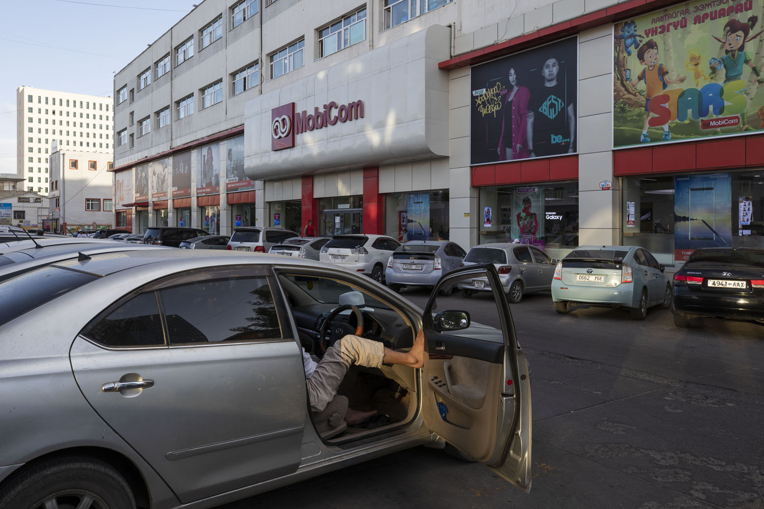 Man sits in a car outside a retail outlet. Ulaanbaatar, Mongolia. 2018.