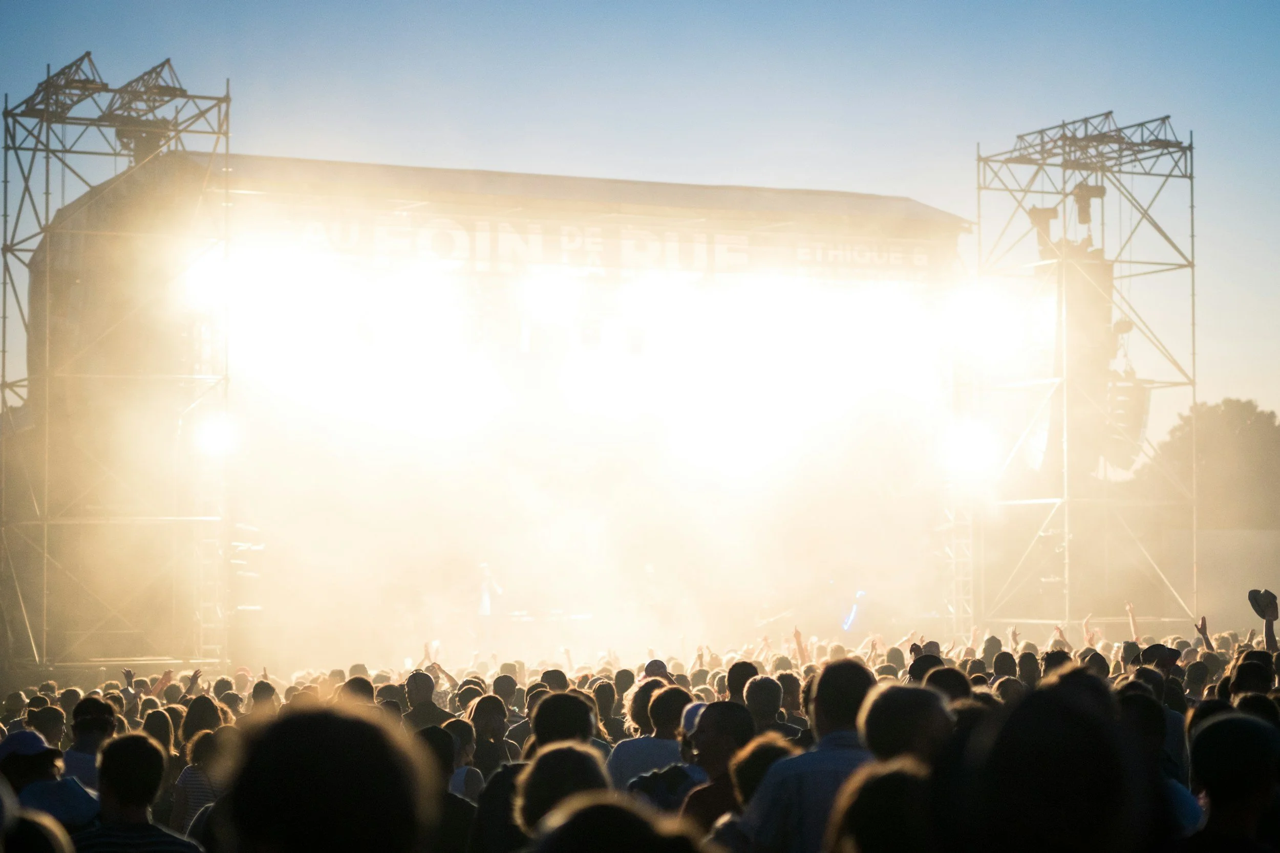 Bright concert stage lit up outside with a crowd full of people watching