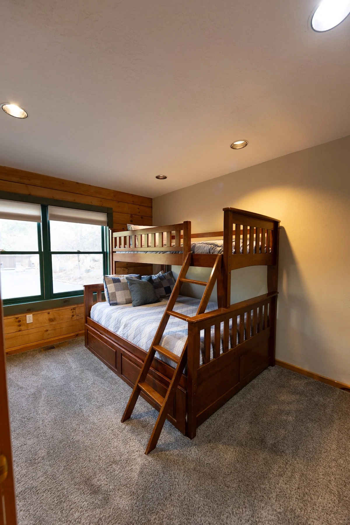 Room with a wooden bunk bed and a window, beige walls, and recessed ceiling lights.