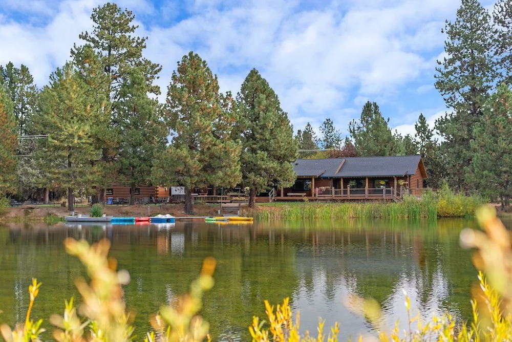 A lake with a wooden house on the shore, surrounded by trees, and canoes floating on the water.