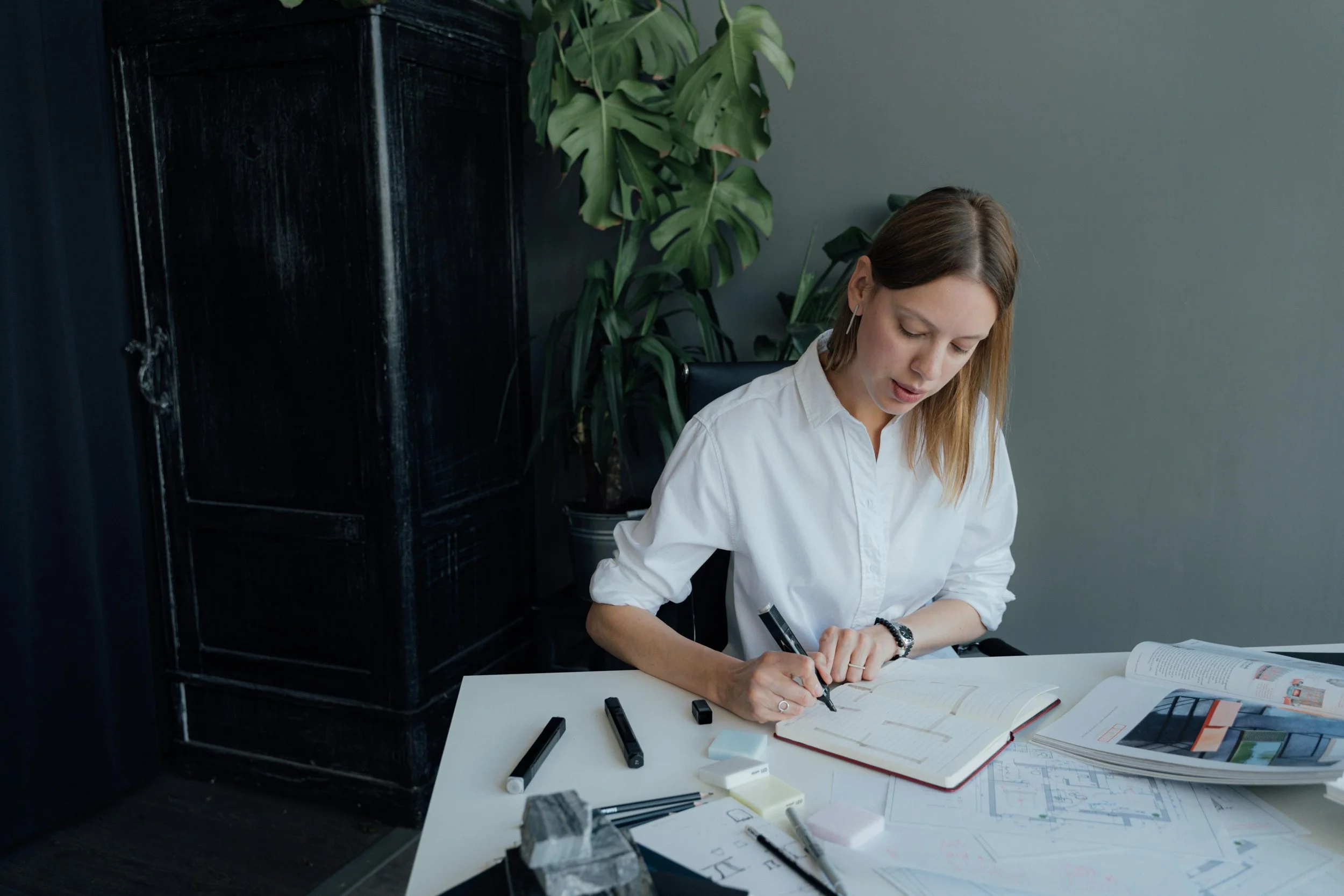 Interior designer sketching floor plans at a modern workspace desk with drawing tools, showcasing the technical precision and spatial planning expertise mentioned in the article