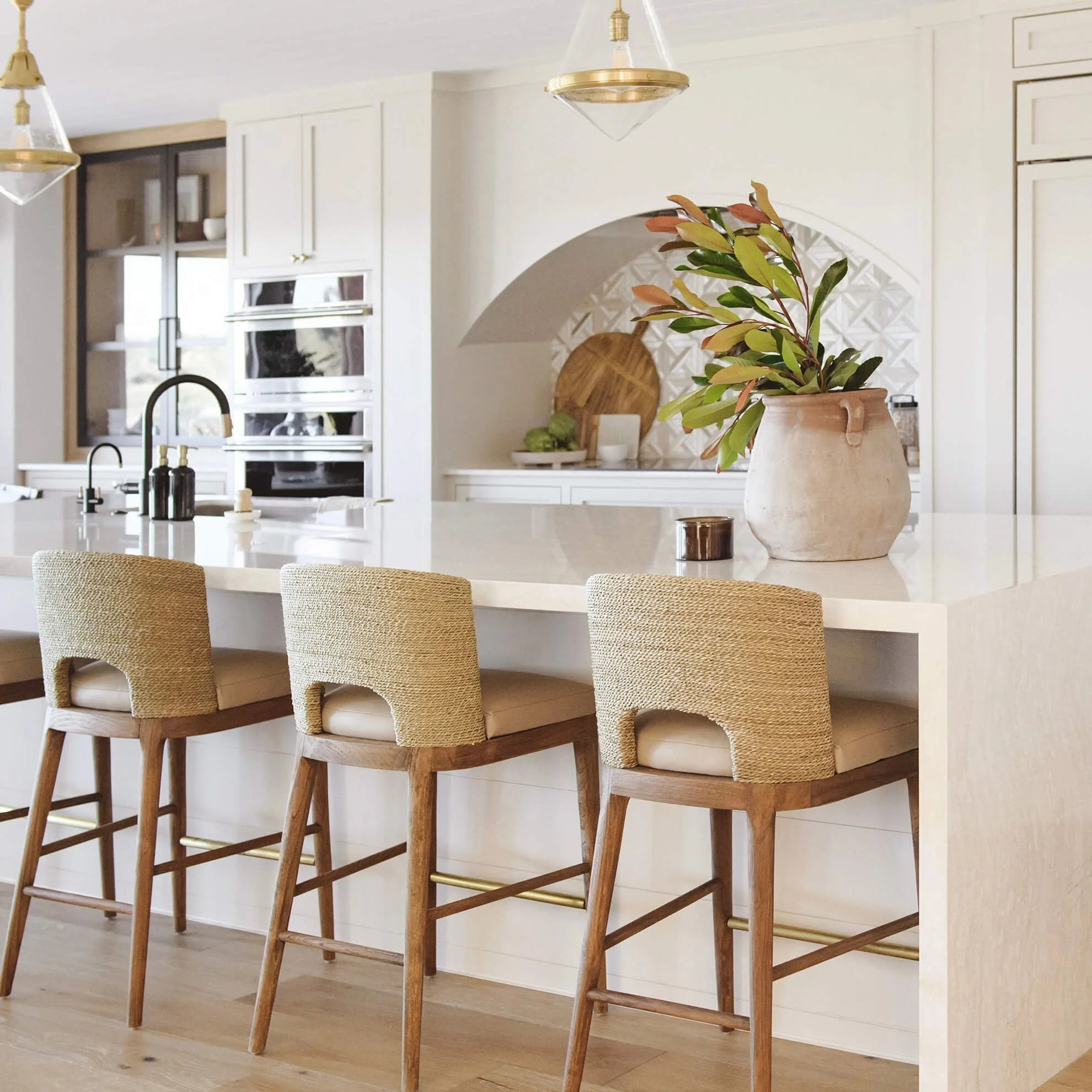 Coastal transitional kitchen island with white quartz countertops, woven bar stools, and arched tile backsplash in a full home remodel by Savvy Interiors in Del Mar, North County San Diego.