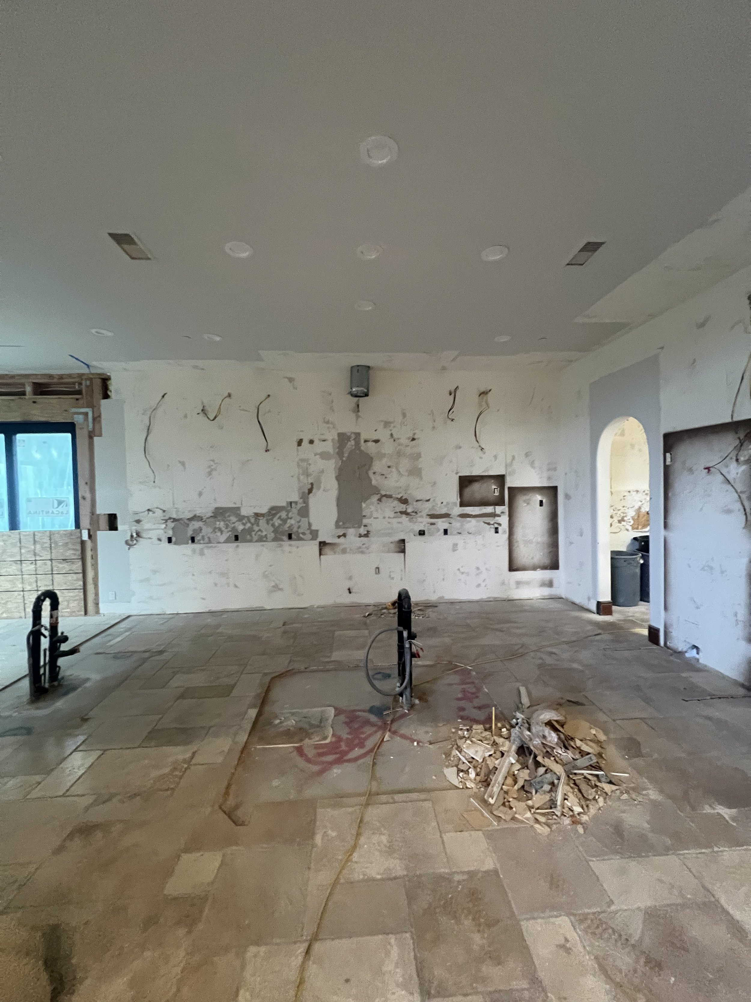 Interior demolition phase of a luxury home renovation by Savvy Interiors in Los Angeles, CA, showing an open living space with exposed wiring, removed finishes, stone flooring, and preparation for a custom kitchen and living area redesign.