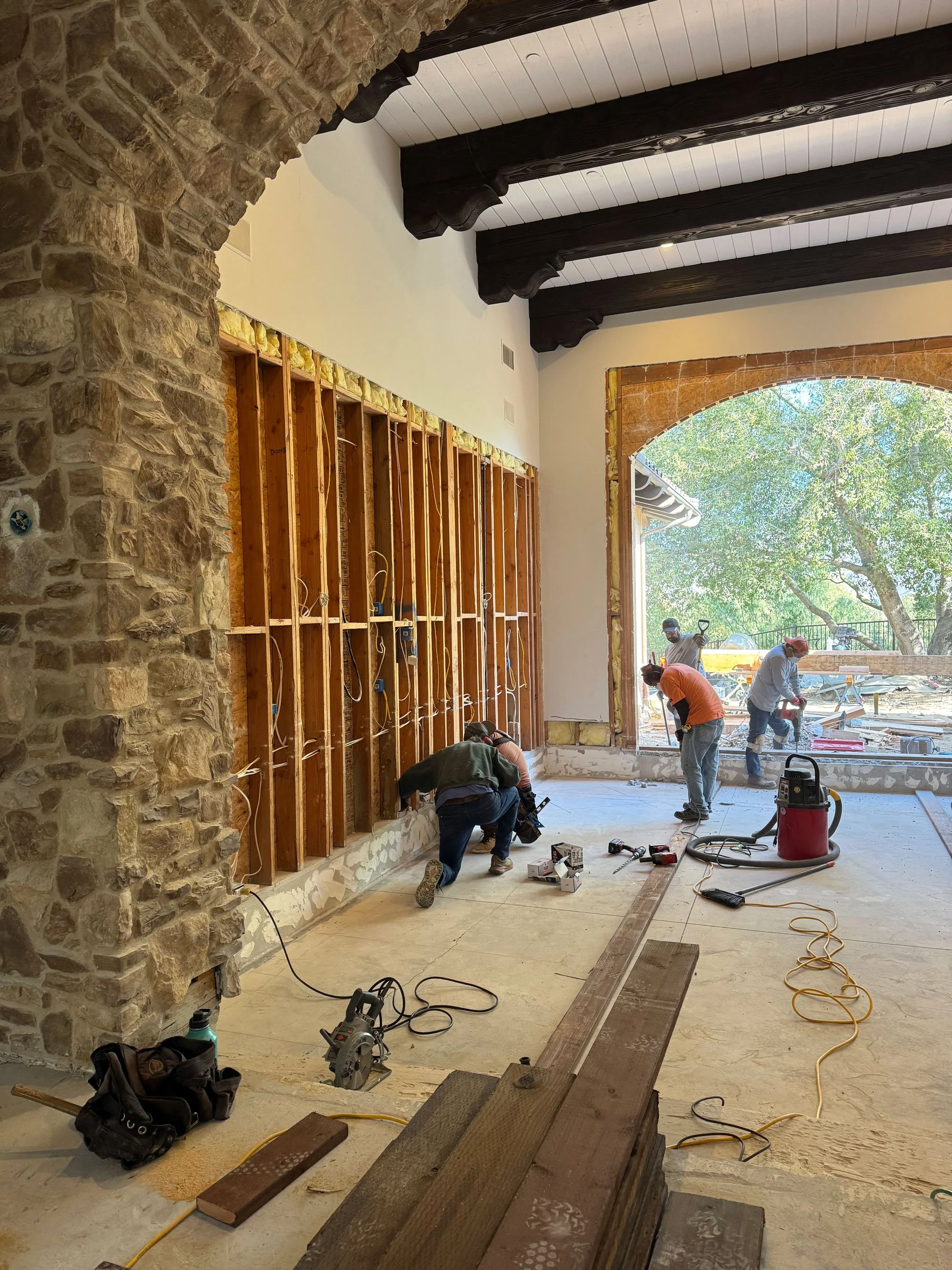 Luxury home renovation in progress by Savvy Interiors in Los Angeles, CA, showing contractors framing interior walls beneath exposed wood ceiling beams and a stone archway during a custom remodel.