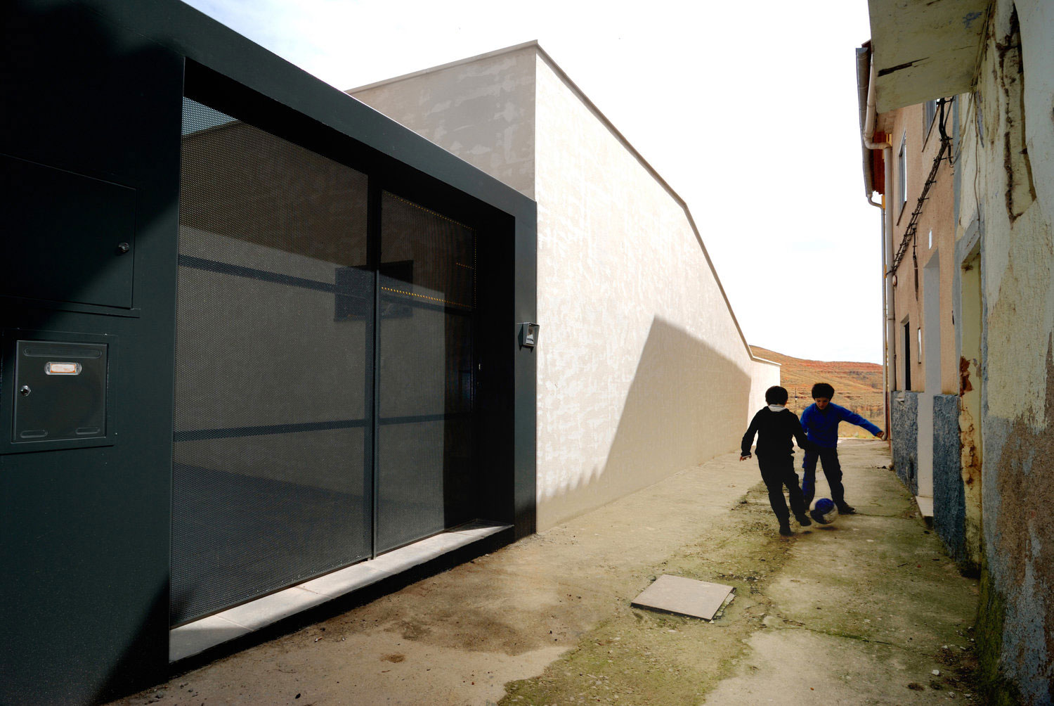 The house is generated from the boundary condition, the place where the landscape becomes aware of itself, a light strip between the consolidated town of a village and the landscape of valleys and ravines, which looks for a higher channel downstream, all chaired by the graceful beauty of the Mudejar Church of Saint Félix. The project strategy consists of exploiting this unique situation linking a residential program with outside through communicating spaces like patios and thick thresholds, which open like gazebos on the landscape, or retreating in private rooms establishing a rich dialogue with the outside and generating new applications that expand the domestic inside. The walls surrounding the site generate three different patios and surface textures on the ground floor being connected with street and urban areas. Two of them are entries, and the other wall generates a private garden which ground floor rooms open to. The house sets back enough to avoid the intrusive vision and the shadow generated by near constructions. The first floor is built as an east-west oriented piece –intimate and separate- that comes away from the inconvenient alignment to improve the characteristics of the terraces in the ground floor crossed block and opens to landscape.