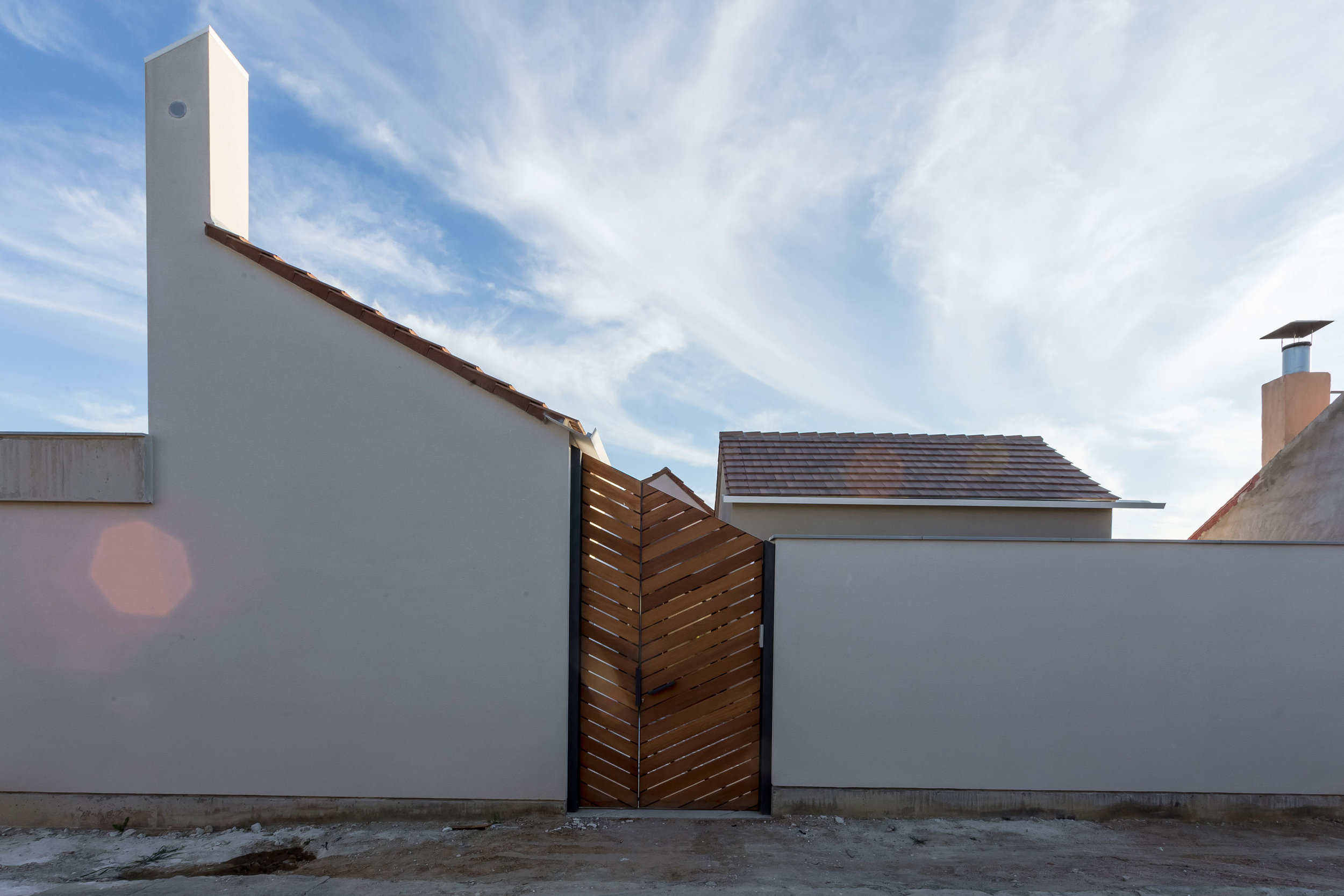 House JI is born in the reinterpretation of the traditional model of housing in this area, Monegros. A hidden house between raised white walls, which looks to the patio inside, is protected from dust and wind, and has relation with the paths and streets nearby through big doors made of wooden boards.