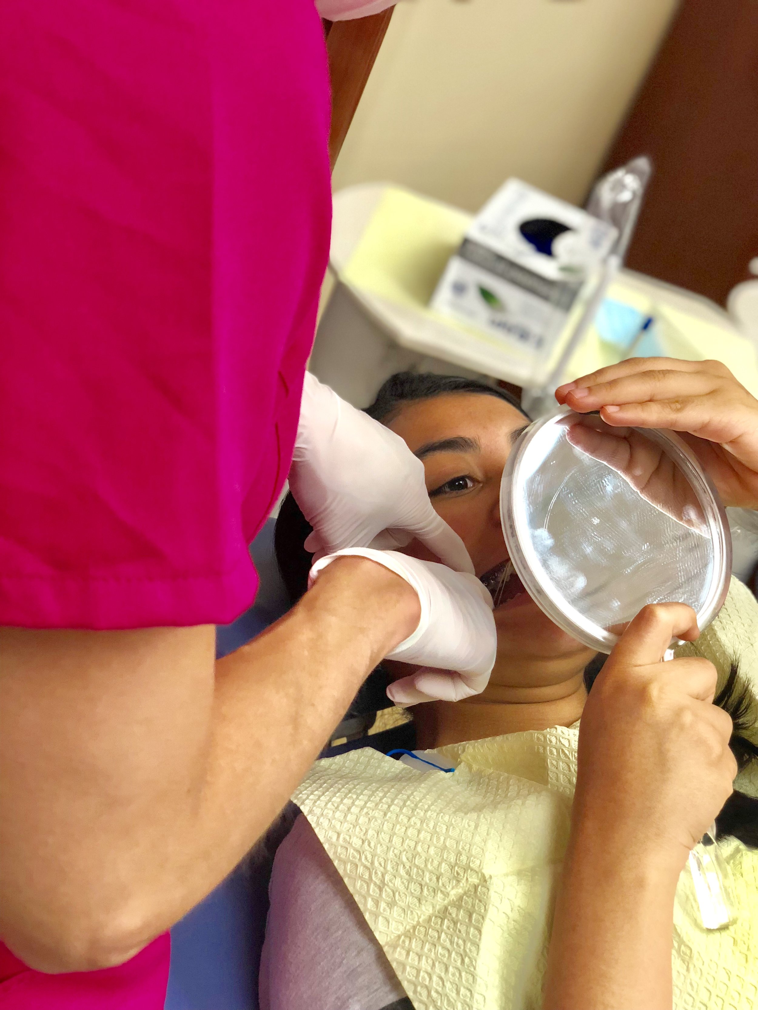 Orthodontic assistant has fingers in a patients mouth as they hold a mirror close to their teeth.