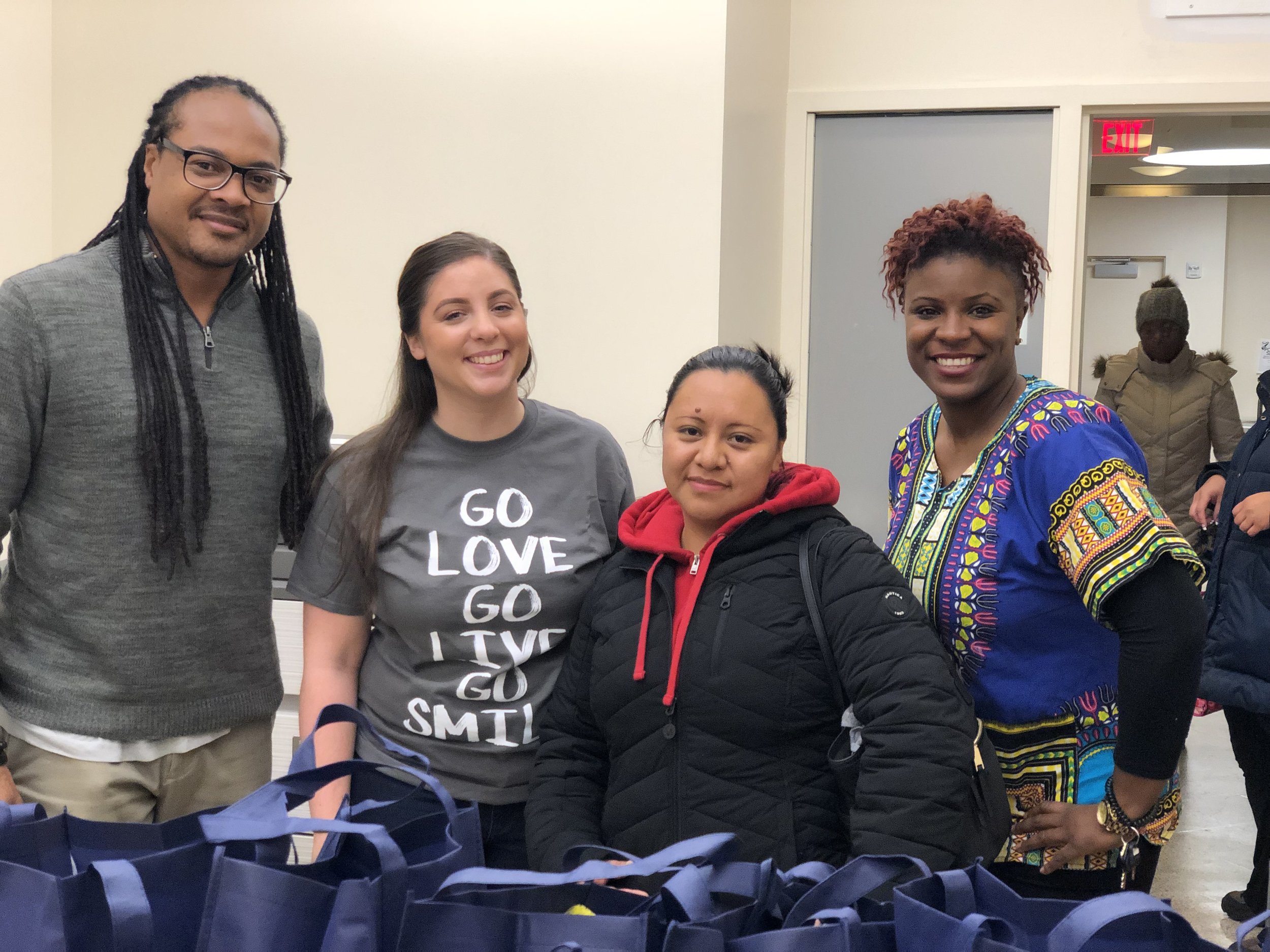 Gerlein staff member stands smiling with members of the donation center. Gerlein bags with donated thanksgiving food items are on the table.