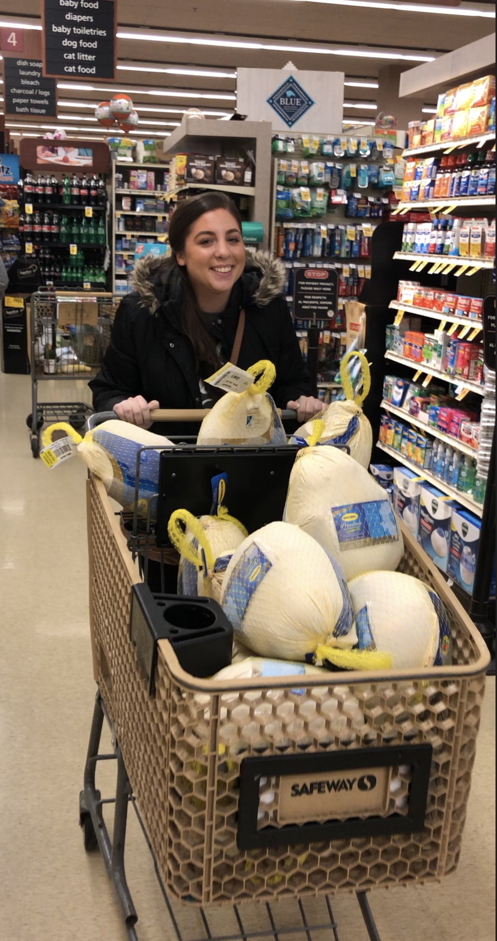 Gerlein team members standing in a grocery store, smiling at the camera,  with a cart full of turkeys to be donated.