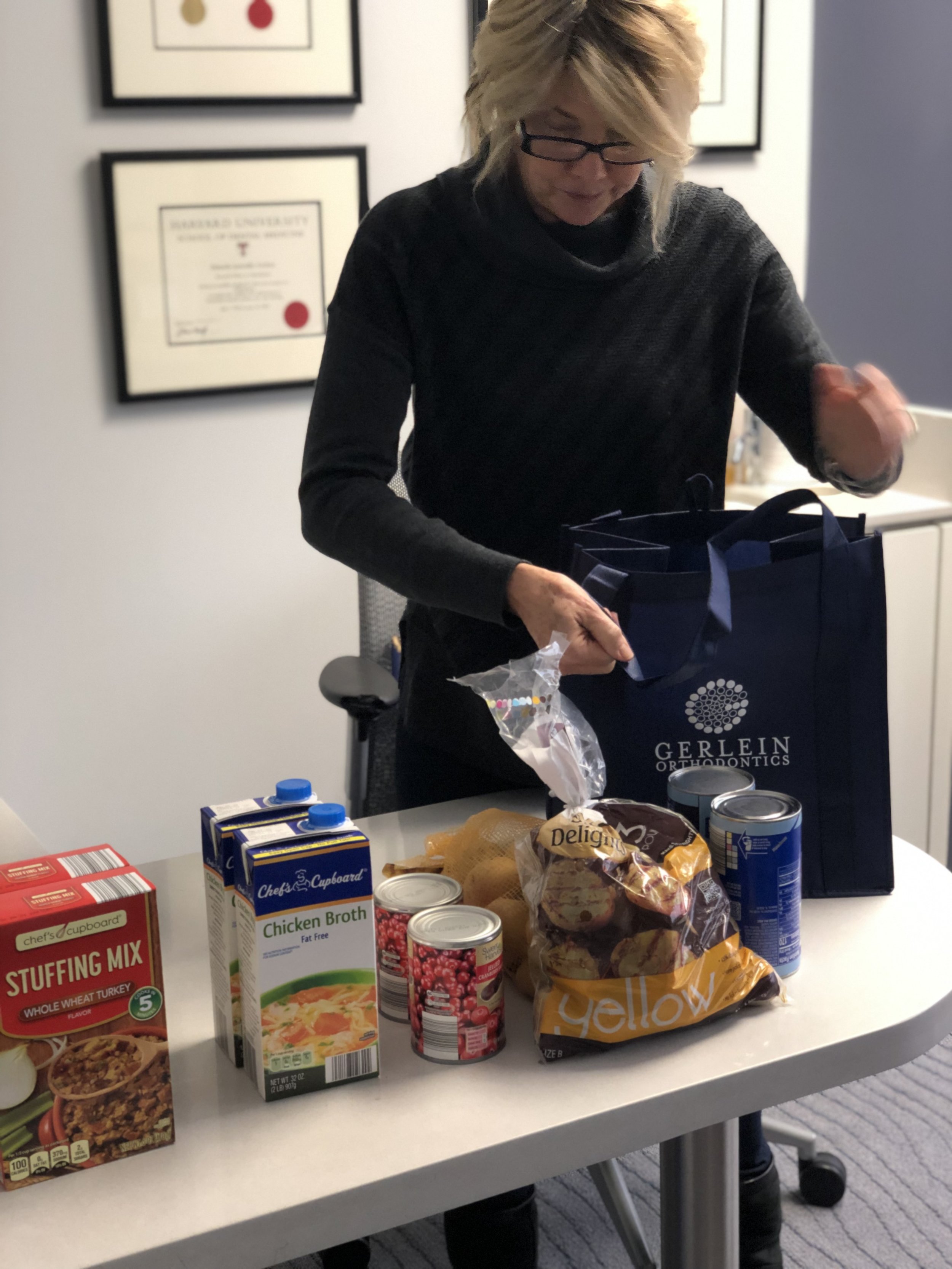 Gerlein team member fills a blue donation bag with thanksgiving food items such as stuffing mix, cranberry sauce, chicken broth, and potatoes. 