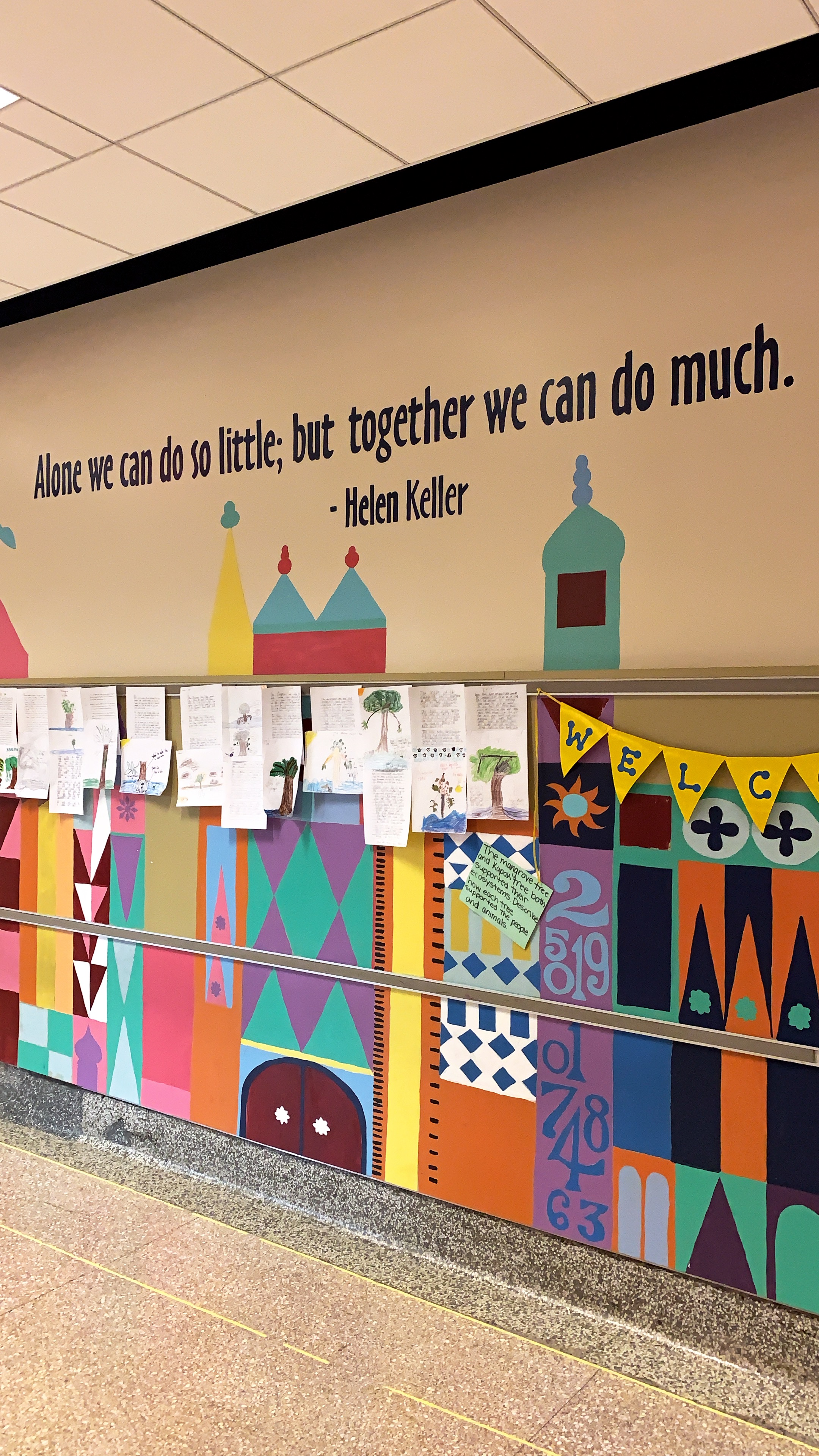 Mural on school wall. Paper cutouts in the shape of buildings below a quote by Helen Keller that says Alone we can do so little, but together we can do much.