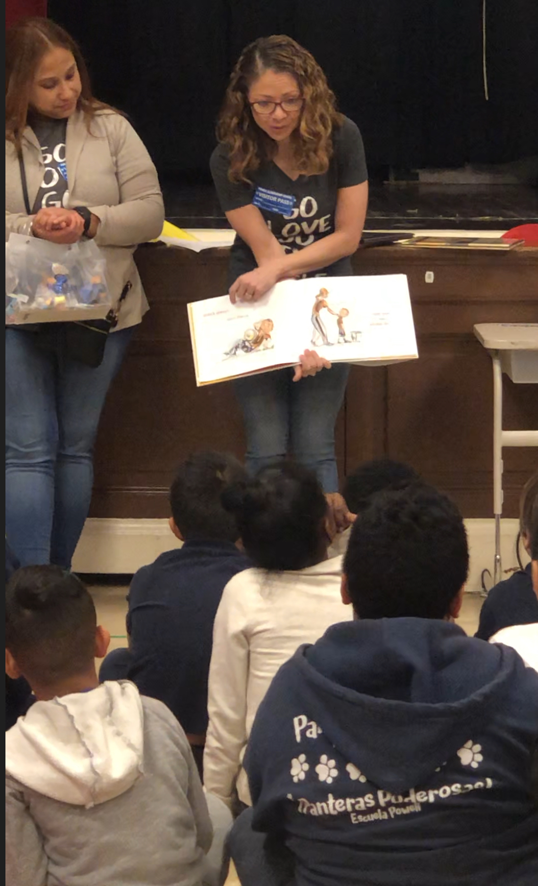 Gerlein team member holding a picture book so that the students in front of her can read what is on the pages 