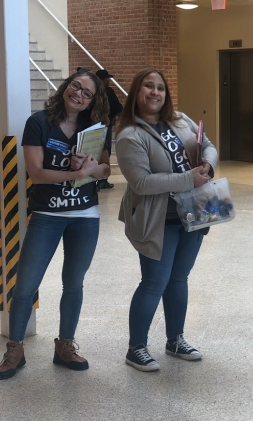 Two Gerlein team members holding books and keychains smile at the camera.