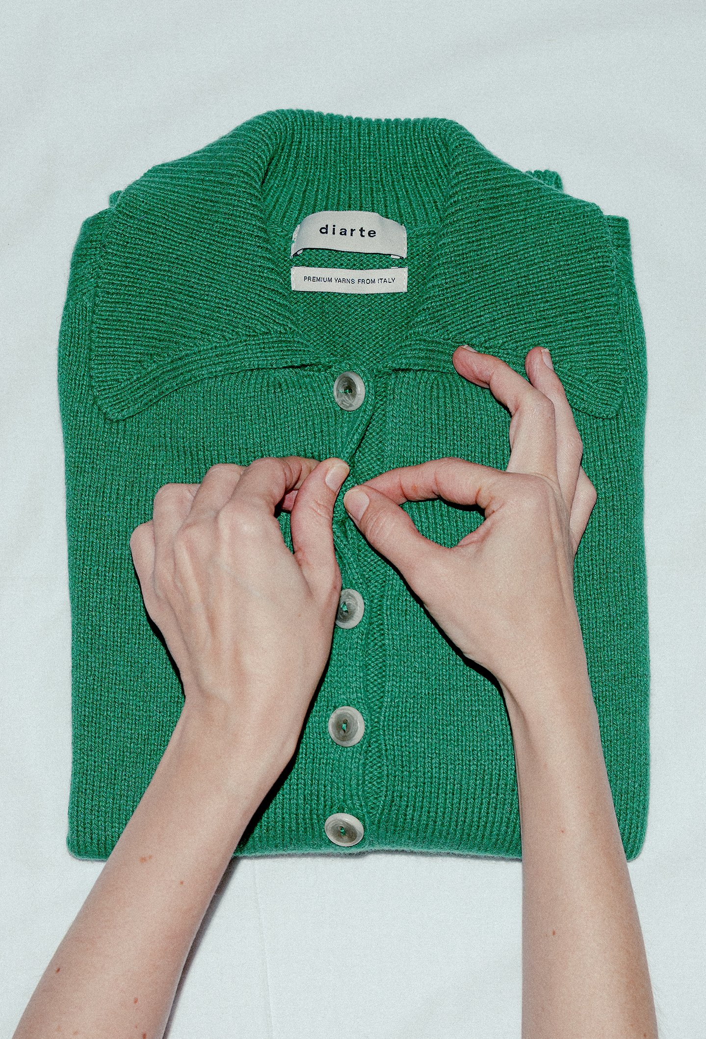 Green knitted cardigan with buttons, being held and displayed by a person's hands.