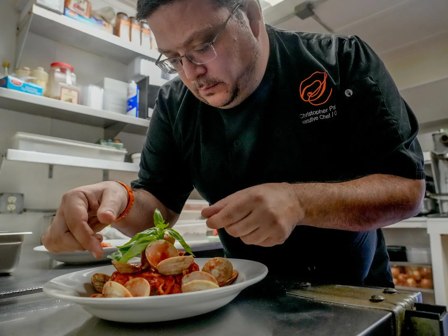 Chef garnishing a plated dish in a professional kitchen.