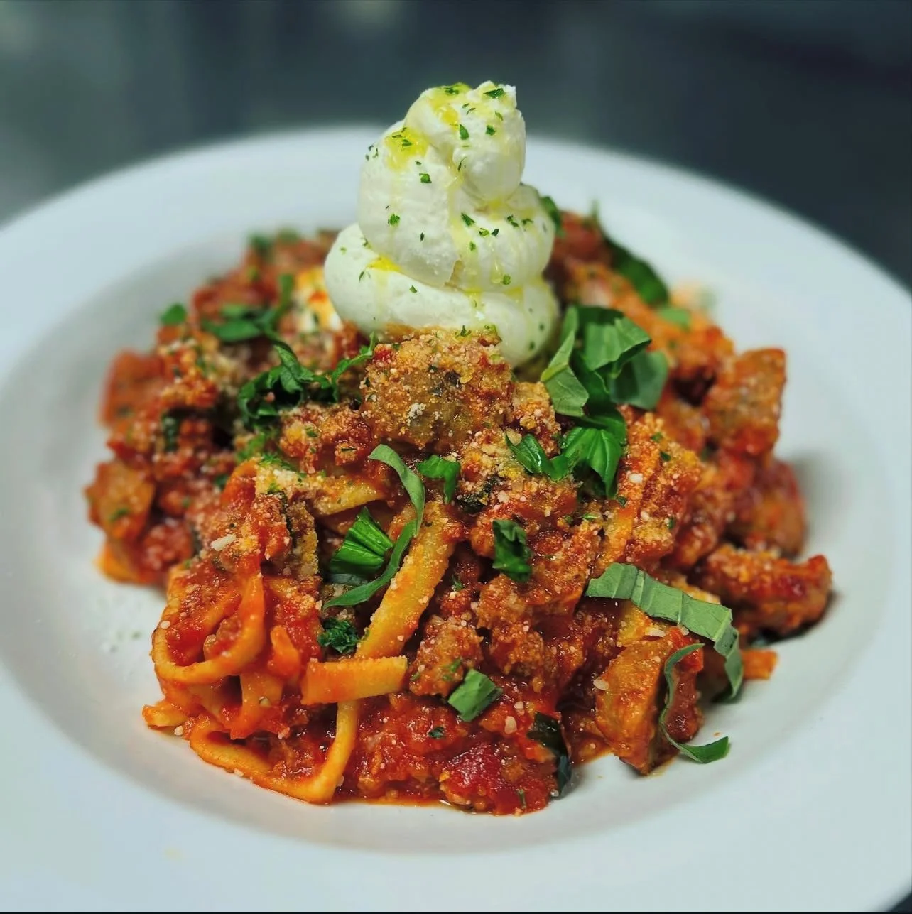 Plate of spaghetti with meat sauce topped with cheese, chopped herbs, and a dollop of sour cream or whipped cream garnished with parsley.