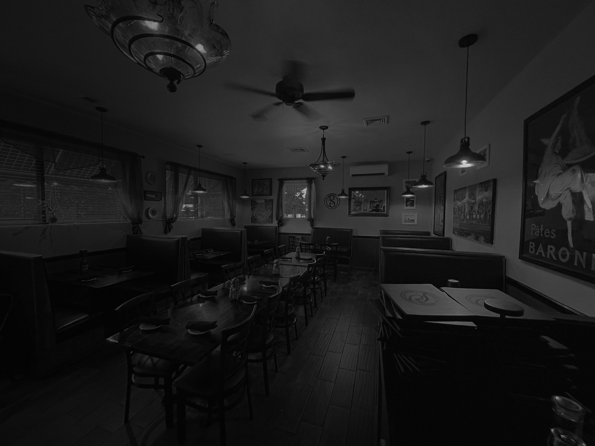 Interior of a dimly lit restaurant with tables and chairs, framed artwork on the walls, and hanging light fixtures.