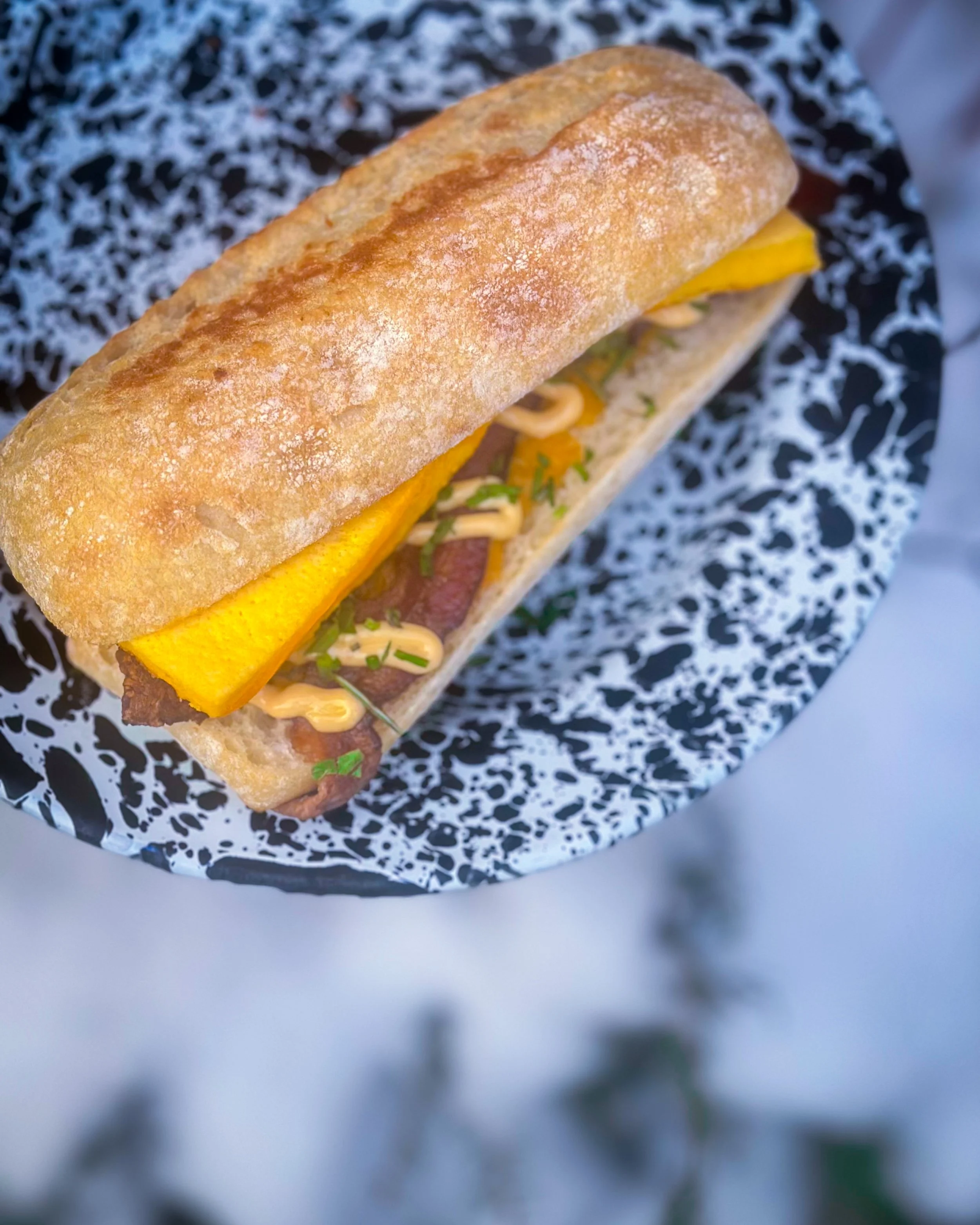Breakfast sandwich on a speckled black and white plate outside of Smallpie.