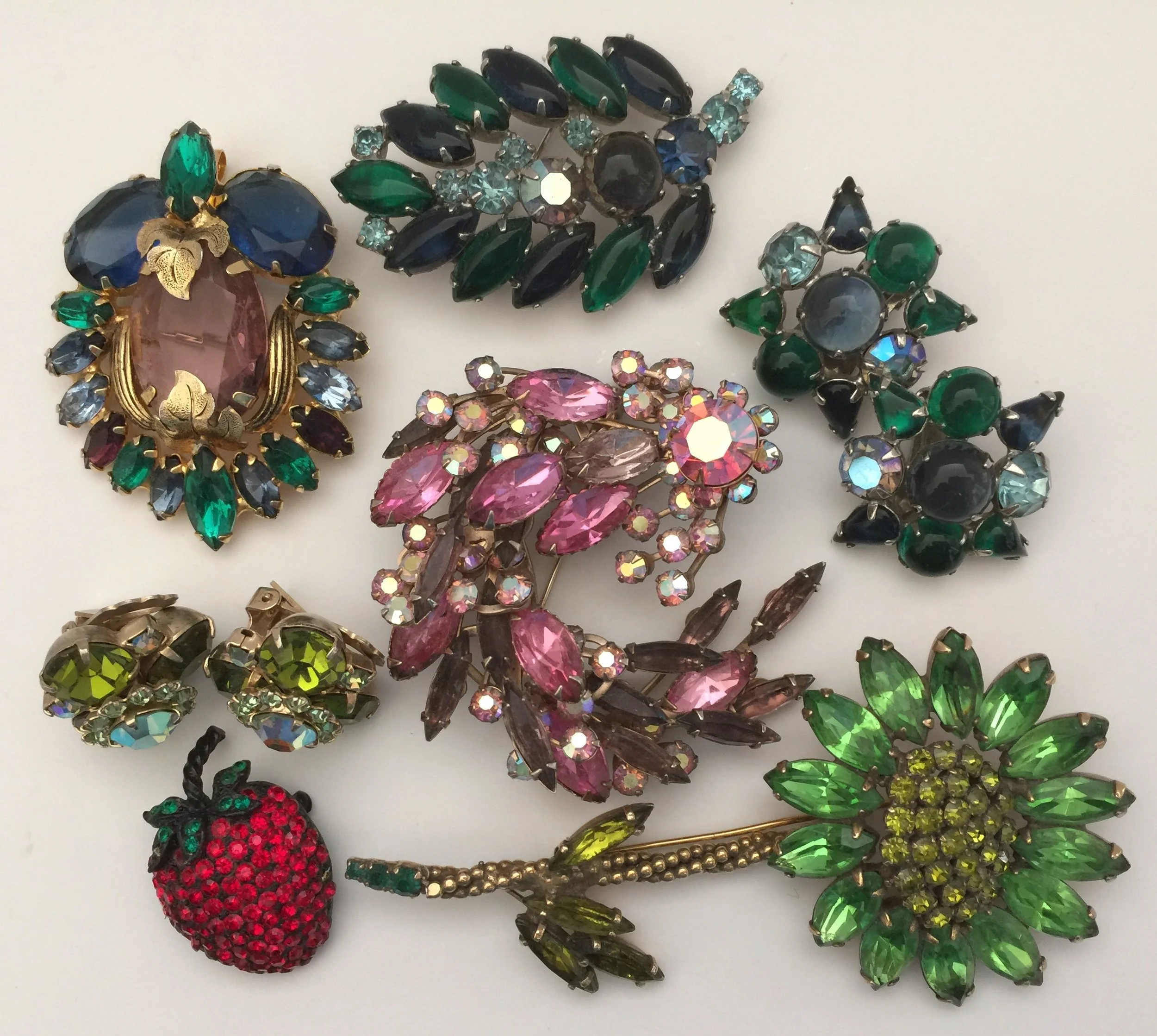 At the top is a beautiful unsigned jeweled pin that is from the 1960s. The blue and green leaf and matching earrings are Weiss from the late 1950s. I bought the large pink jeweled pin in the mid 1960s to wear on a pink satin formal dress that I made to wear to a special banquet with my future husband. I wore the beautiful Weiss green flower pin and the unsigned earrings with a green silk dress. The little Weiss strawberry is from the early 1960s and has always been a favorite of mine that I still wear.