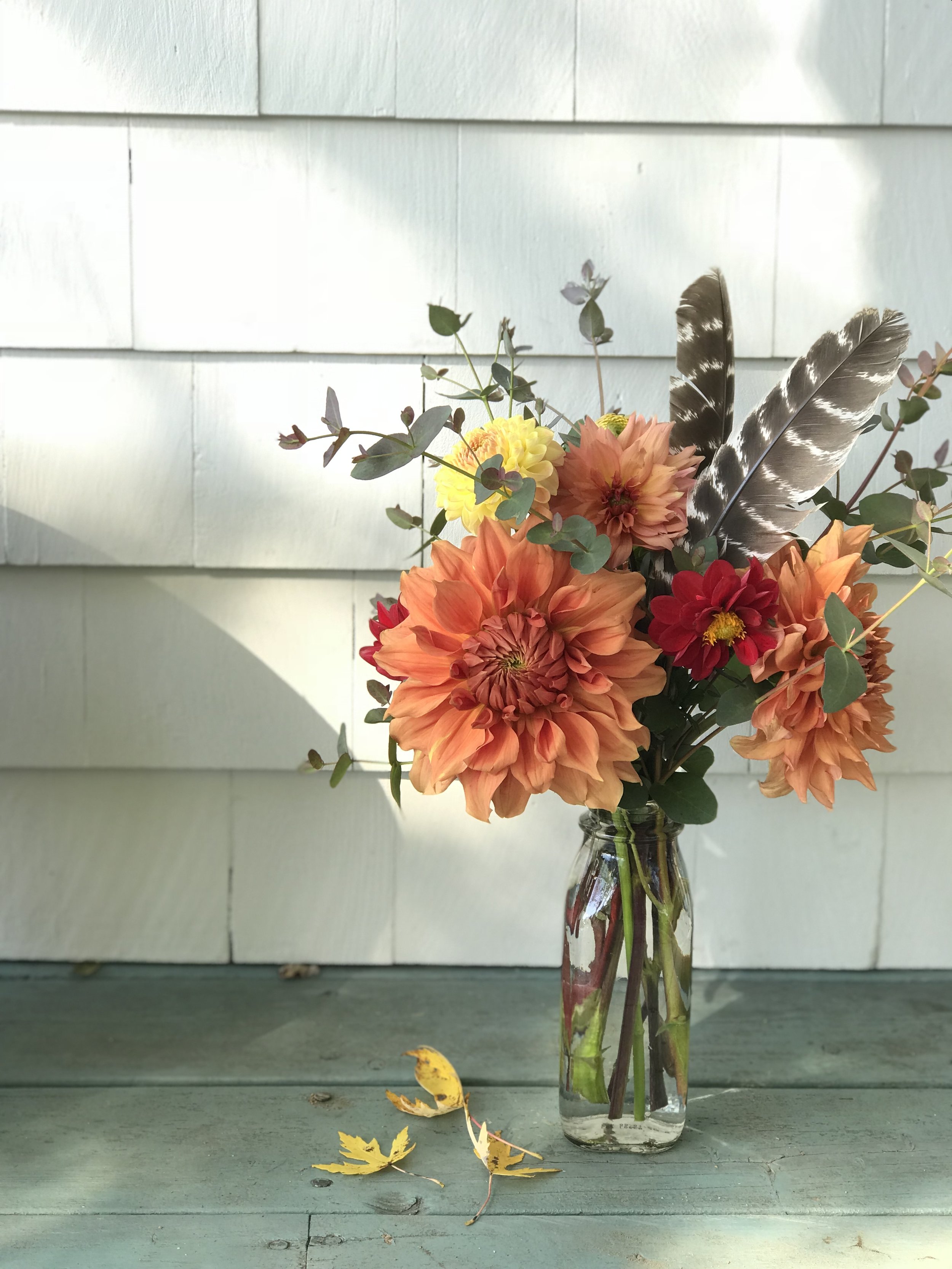 small vase arrangement featuring orange dahlias and turkey feathers