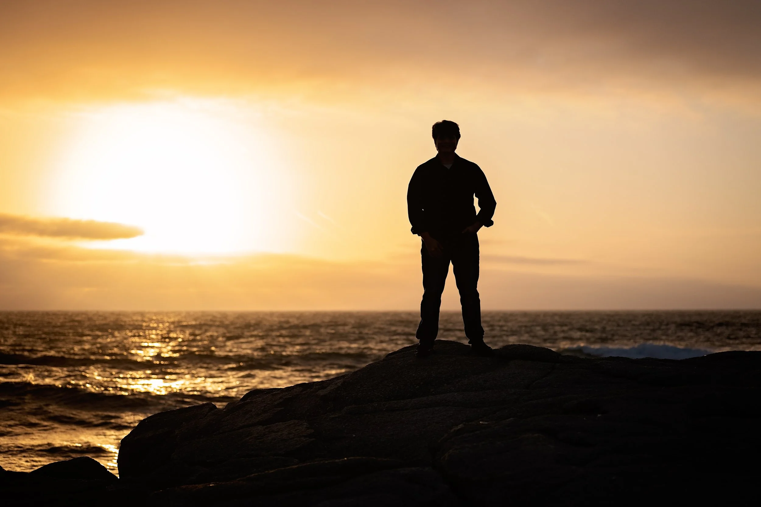 Silhouette of Salinas High School graduate Gianni standing on coastal rocks at sunset at Asilomar in Pacific Grove.