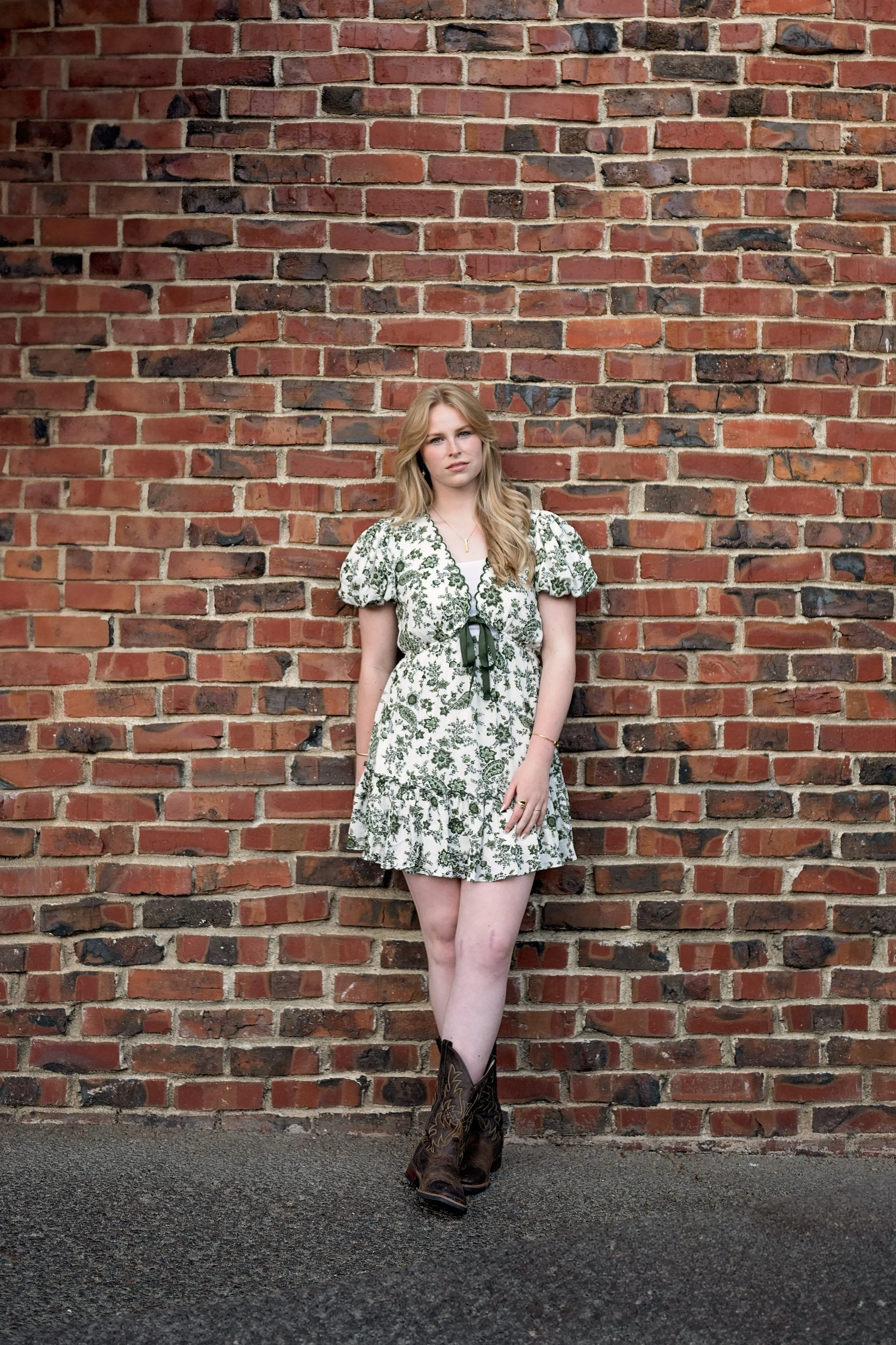 Camden wearing cowboy boots and a green floral dress for senior pictures in a Carmel garden