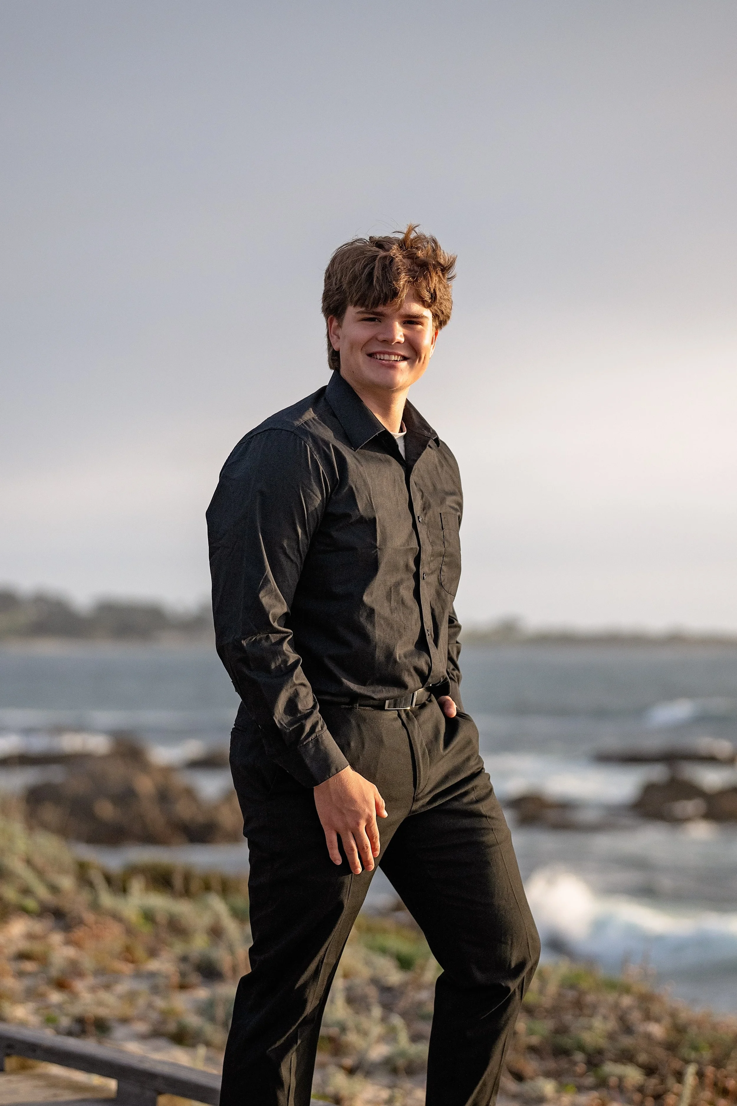 Senior portrait of Gianni in a black dress shirt along the rocky Pacific Grove coastline at Asilomar.