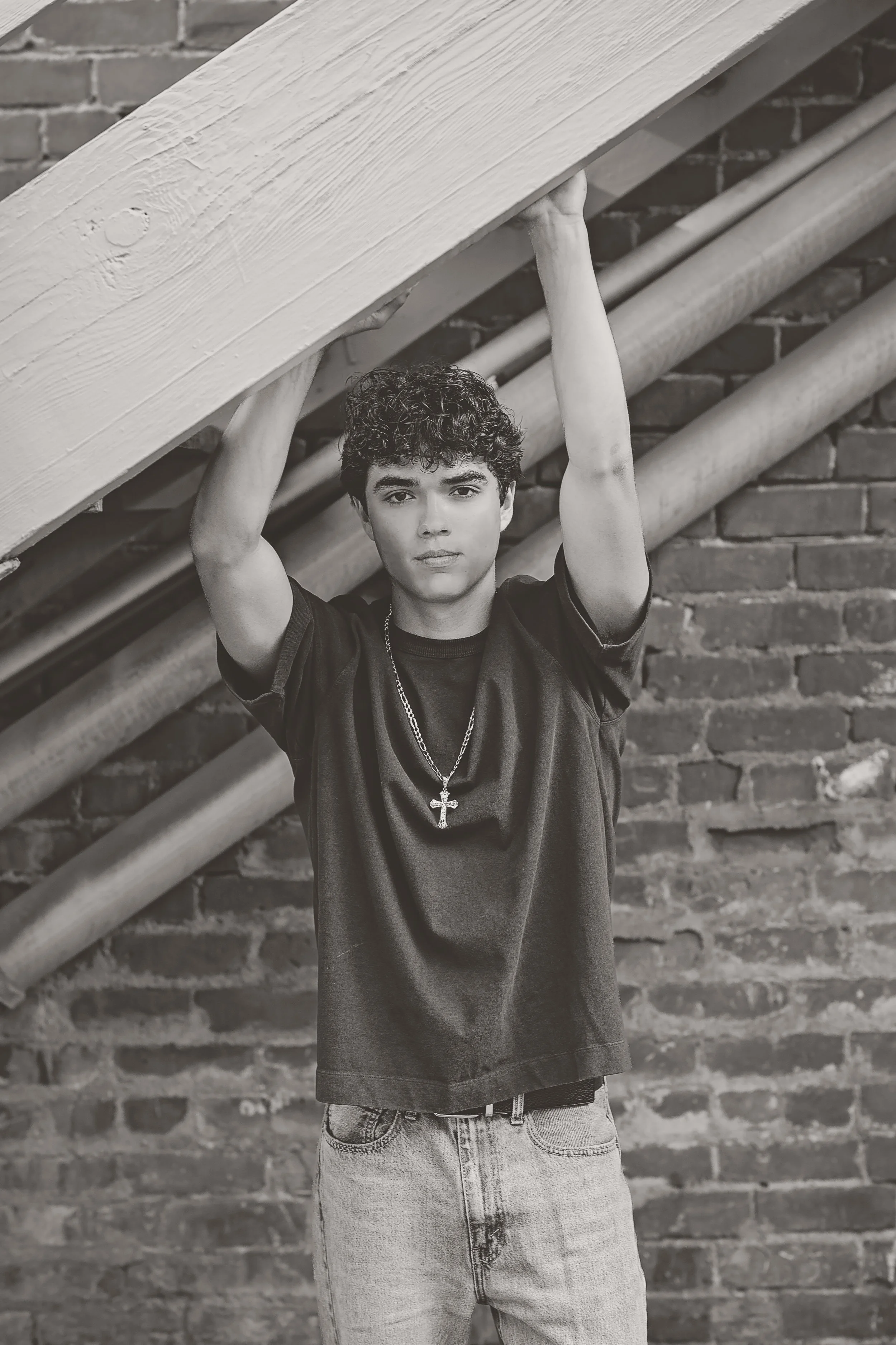 Black-and-white senior portrait of Cruz beneath an outdoor staircase against a historic brick building in Downtown Salinas.