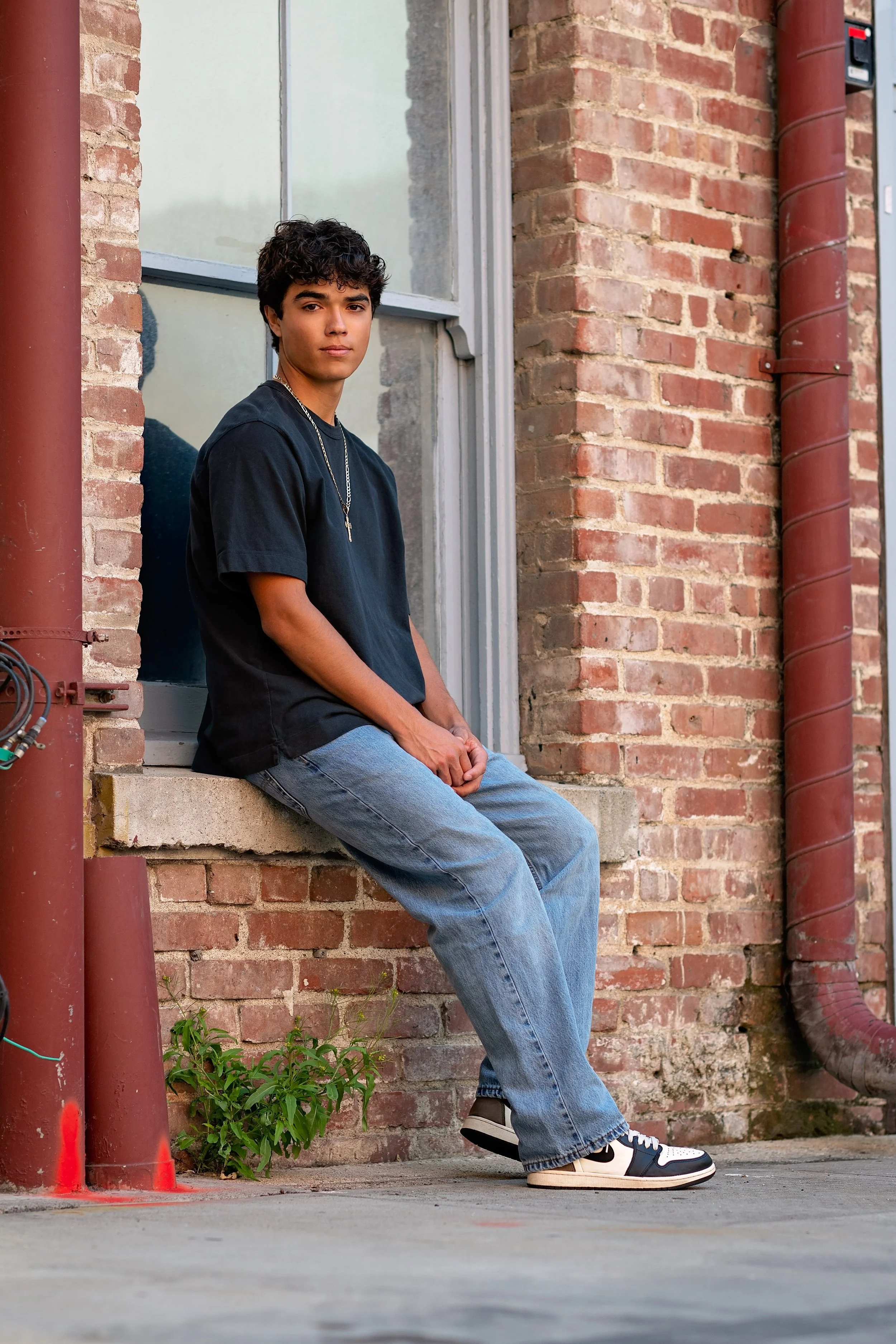 Cruz sitting beside a window and historic brick wall during his senior portrait session in Downtown Salinas, California.