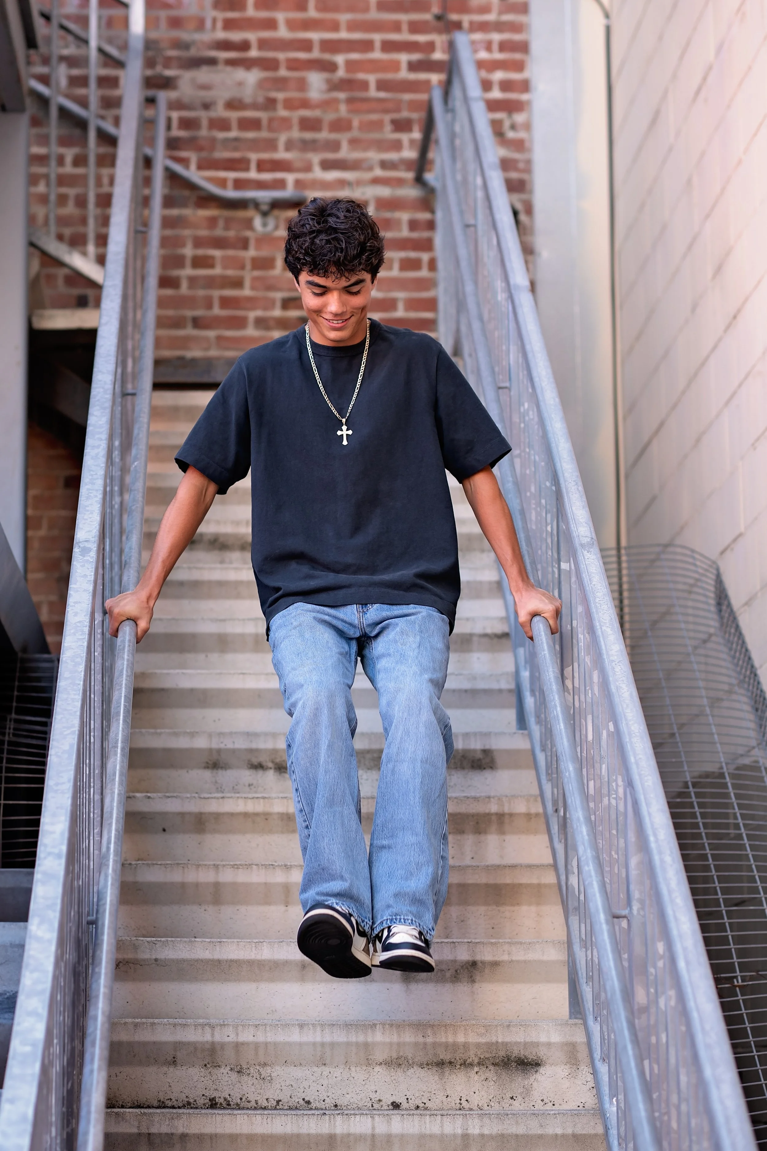 Cruz walking down an outdoor staircase in jeans and a black shirt during his Salinas senior portrait session.