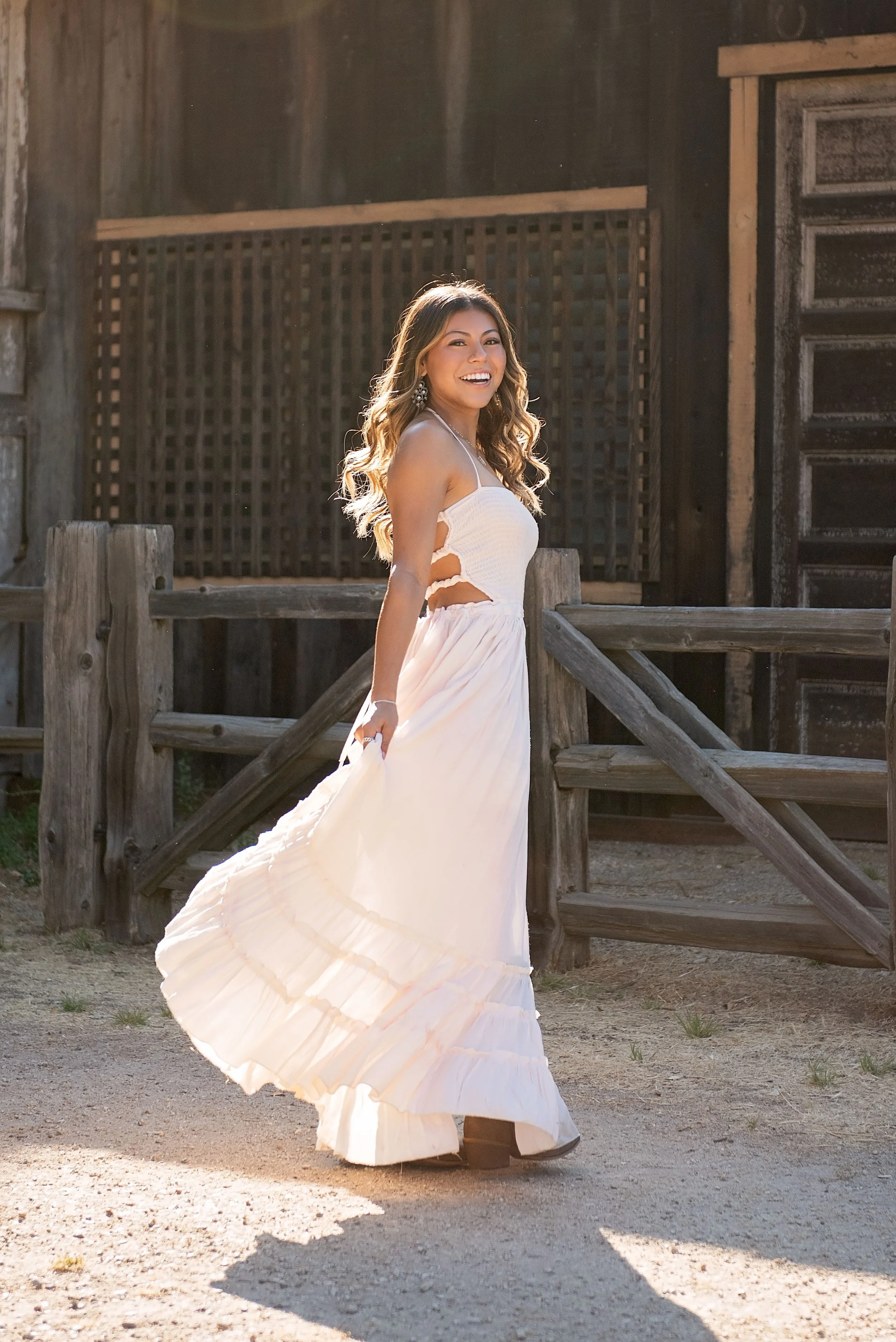 Salinas High senior Aubrey twirling her white dress in front of a rustic barn at Garland Ranch