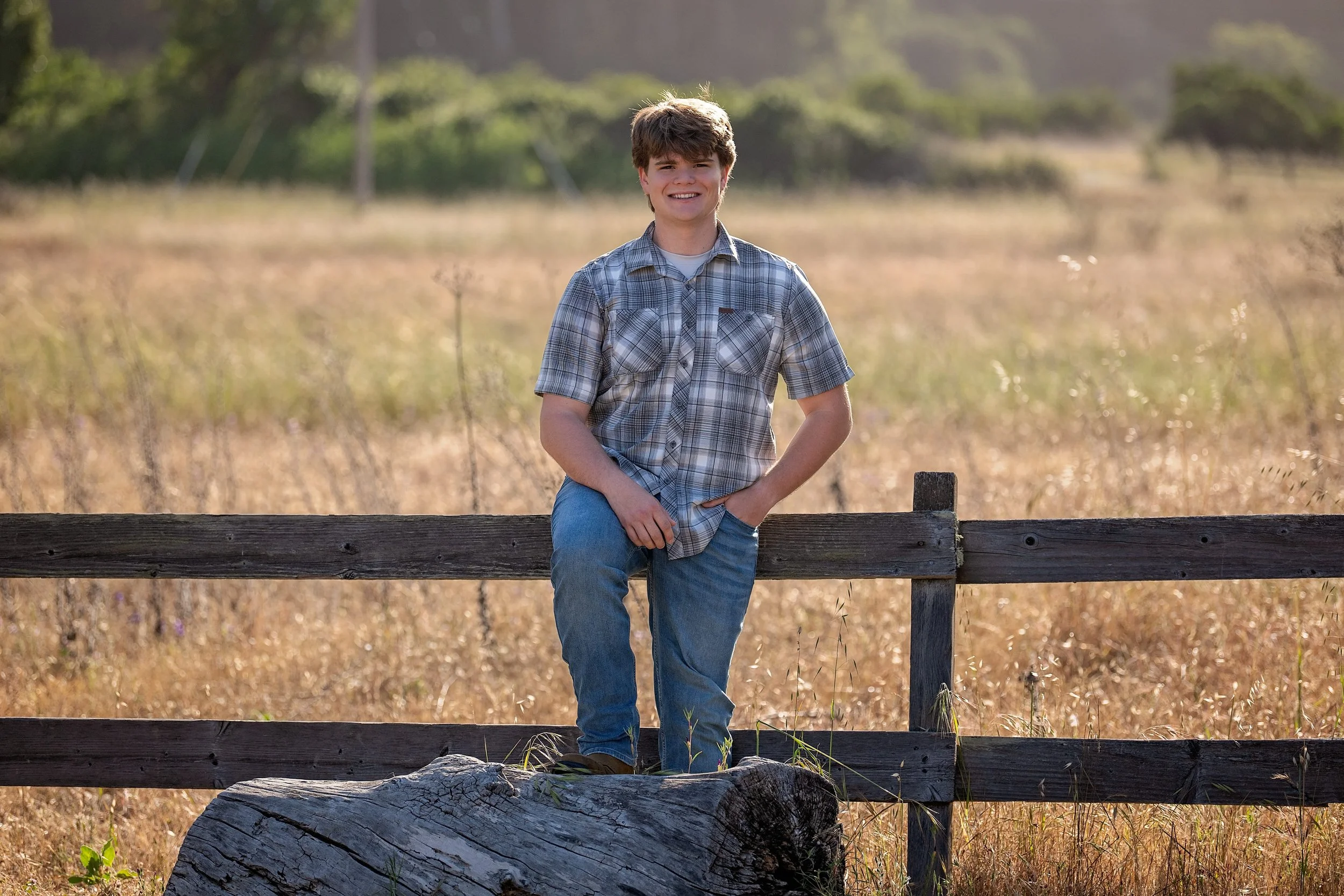 Senior portrait of Gianni leaning against a wooden fence in a golden Carmel Valley field.