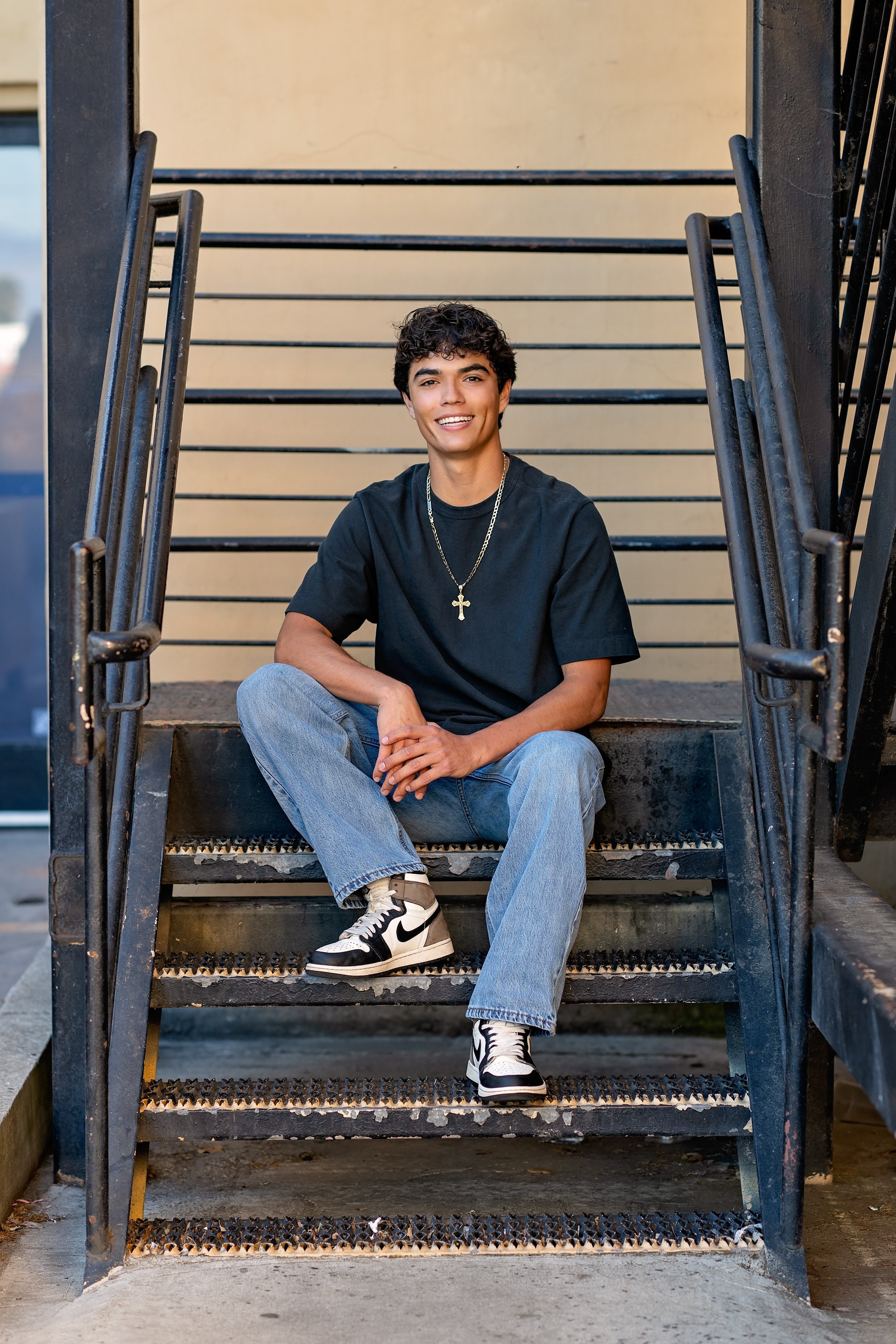 Salinas High School senior Cruz sitting on an industrial staircase during his Downtown Salinas senior portrait session.