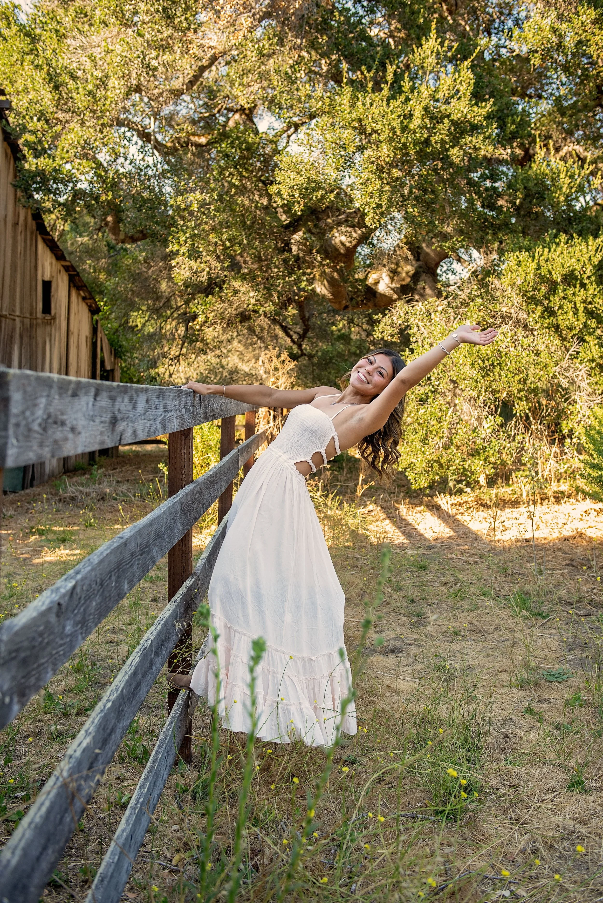 Aubrey laughing beside a rustic fence during her senior pictures at Garland Ranch in Carmel Valley