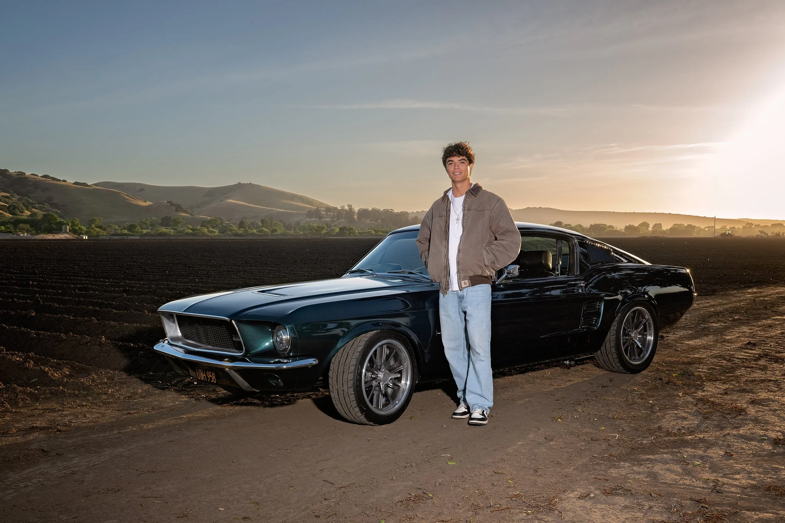Cruz standing beside his vintage Ford Mustang at sunset in Spreckels, California during his senior portrait session.