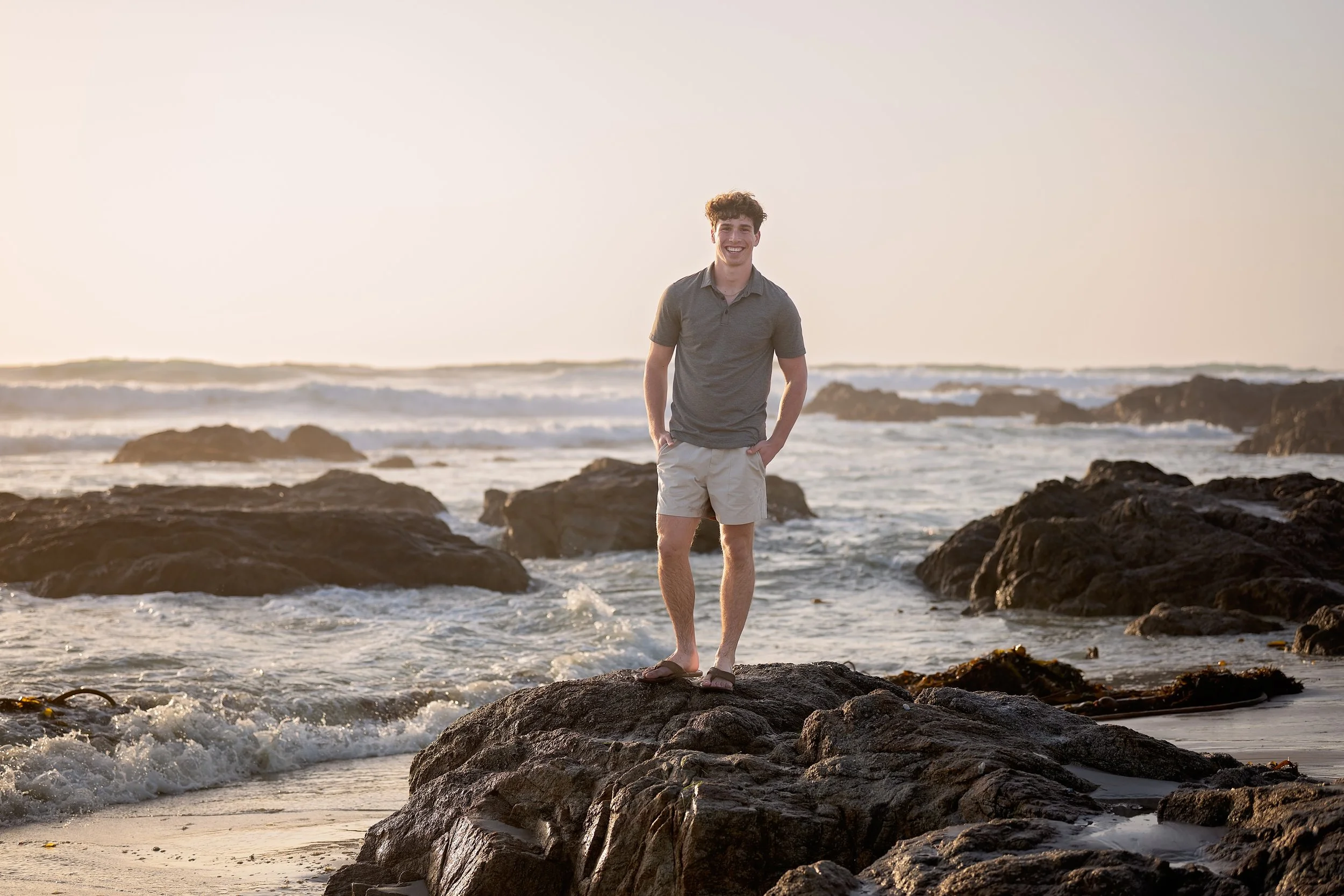 boy in polo shirt and shorts standing on the rocks in the surf on a beach in Monterey, ca