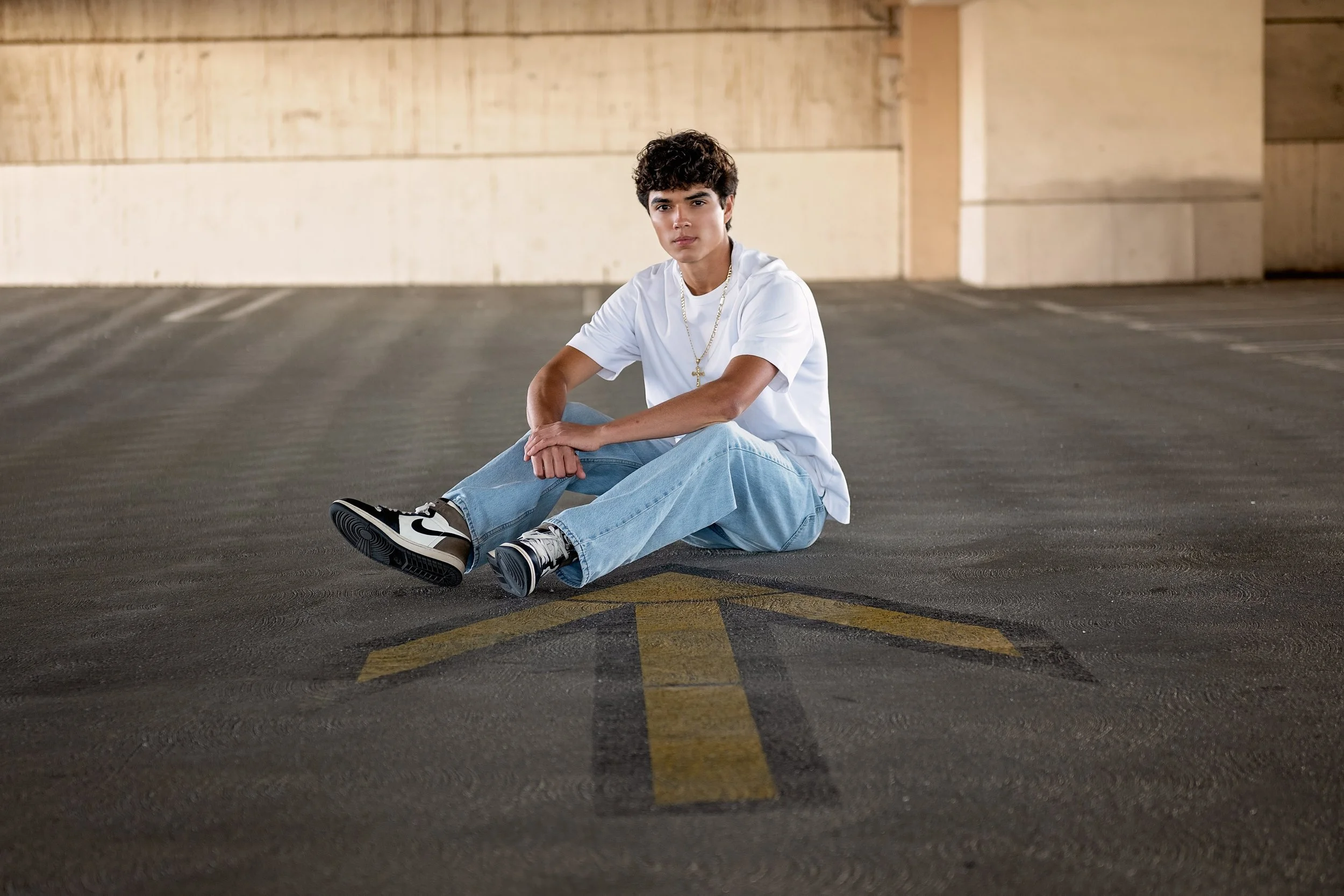 Cruz sitting in a Salinas parking garage during his senior portrait session wearing a white shirt and jeans.