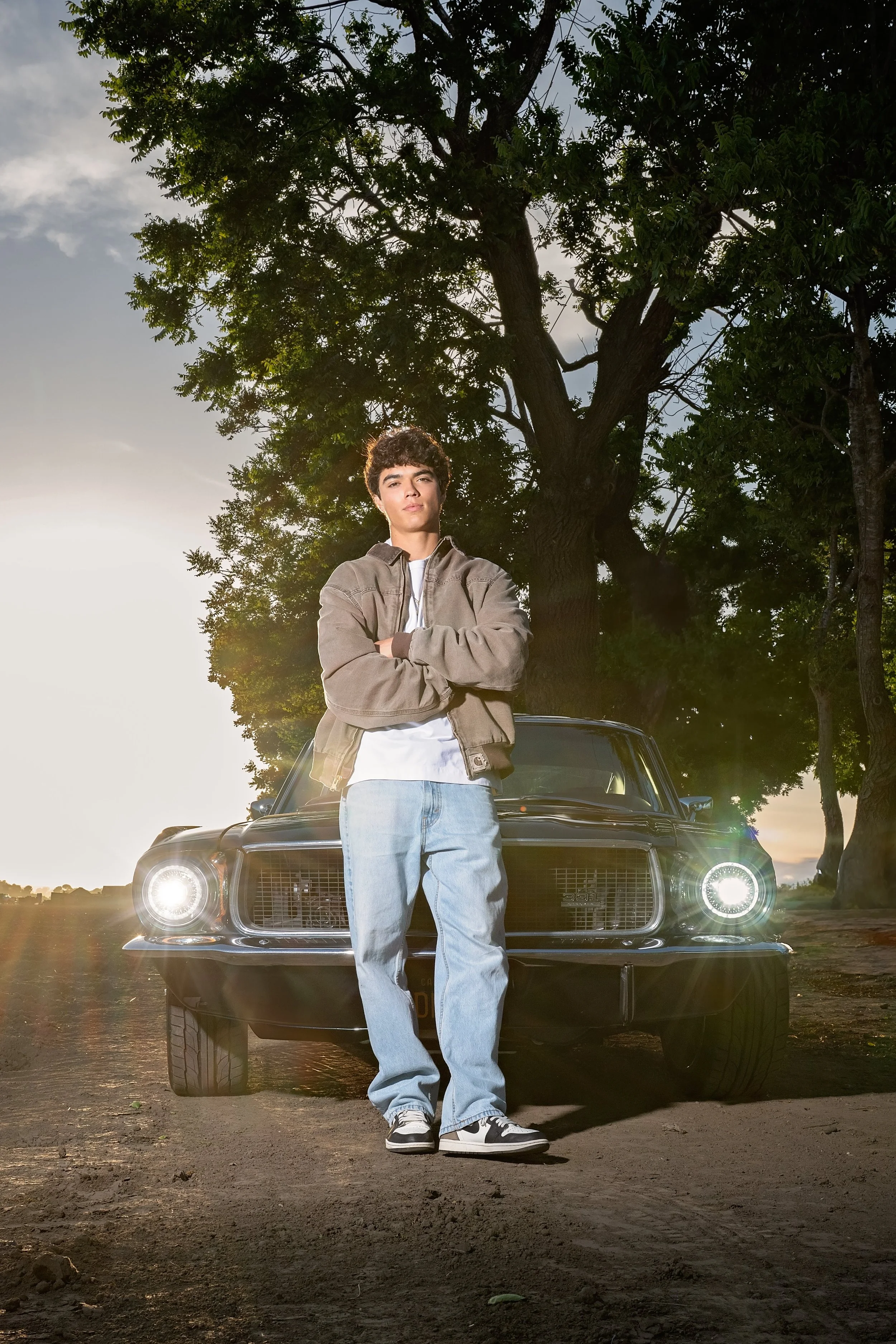 Salinas High School graduate Cruz standing in front of his vintage Mustang with the headlights on at sunset.