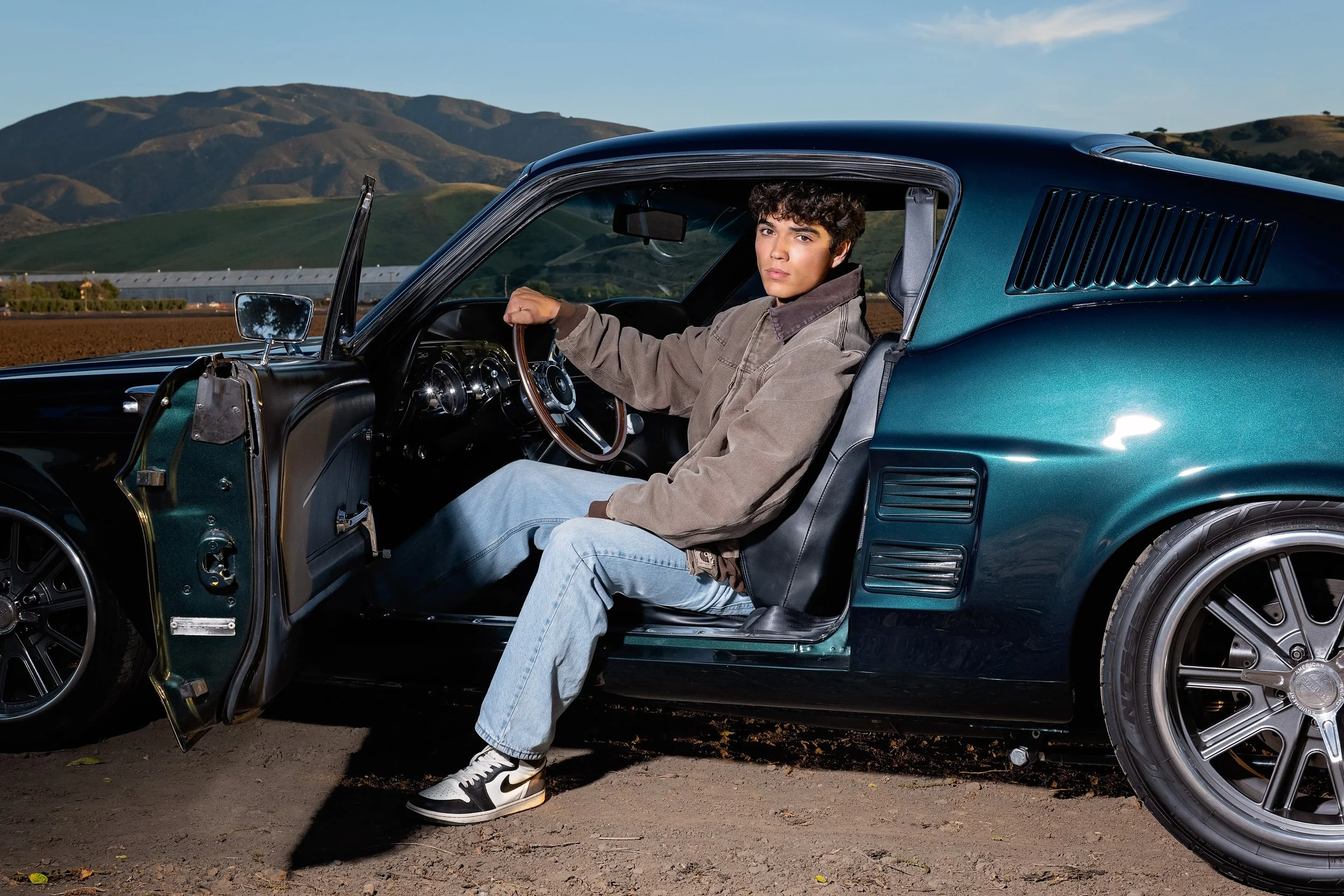 Cruz sitting in the driver’s seat of his vintage Ford Mustang with Salinas Valley hills in the background.