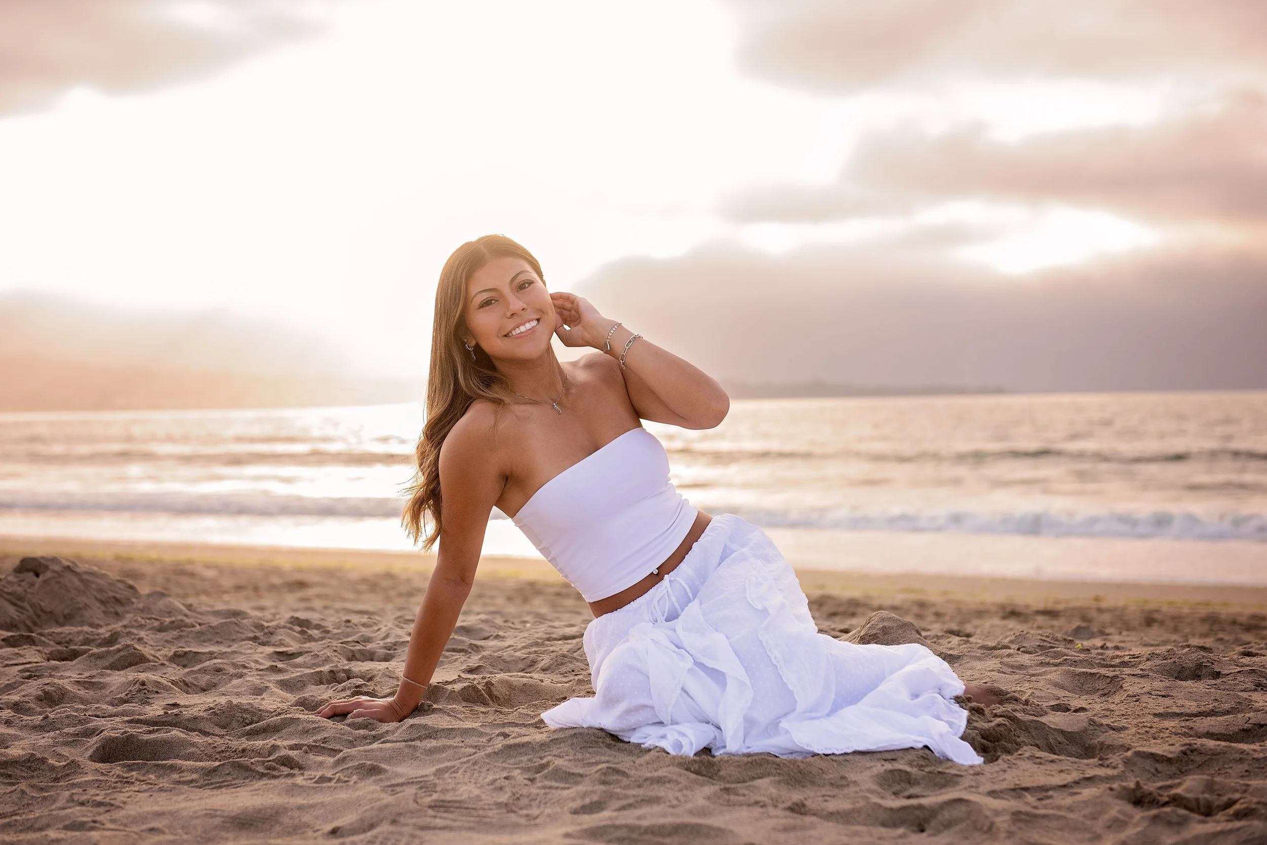 Sunset senior portrait of Aubrey sitting on the sand at Del Monte Beach in Monterey