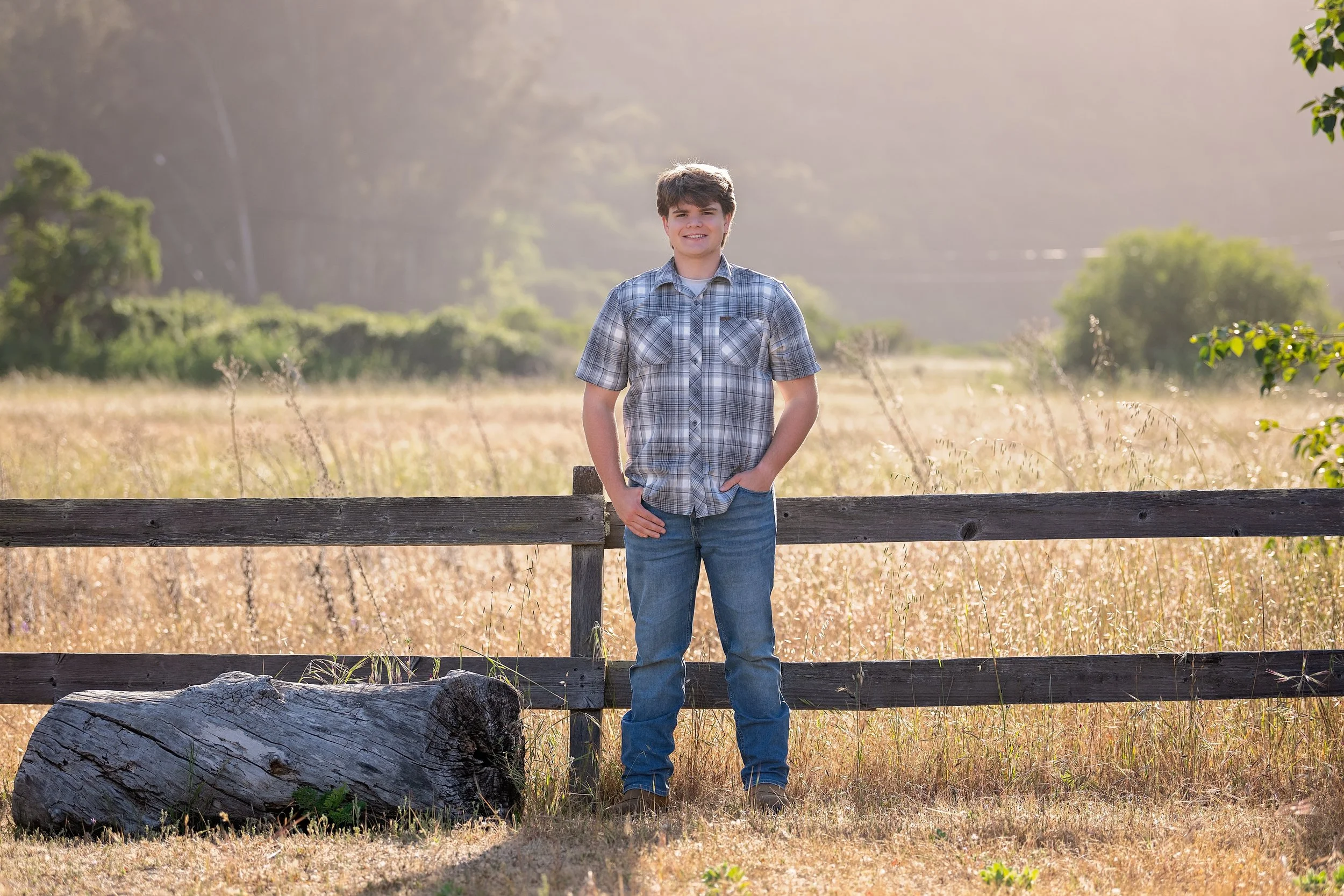 Gianni standing beside a rustic wooden fence during his senior portrait session at Garland Ranch in Carmel Valley.