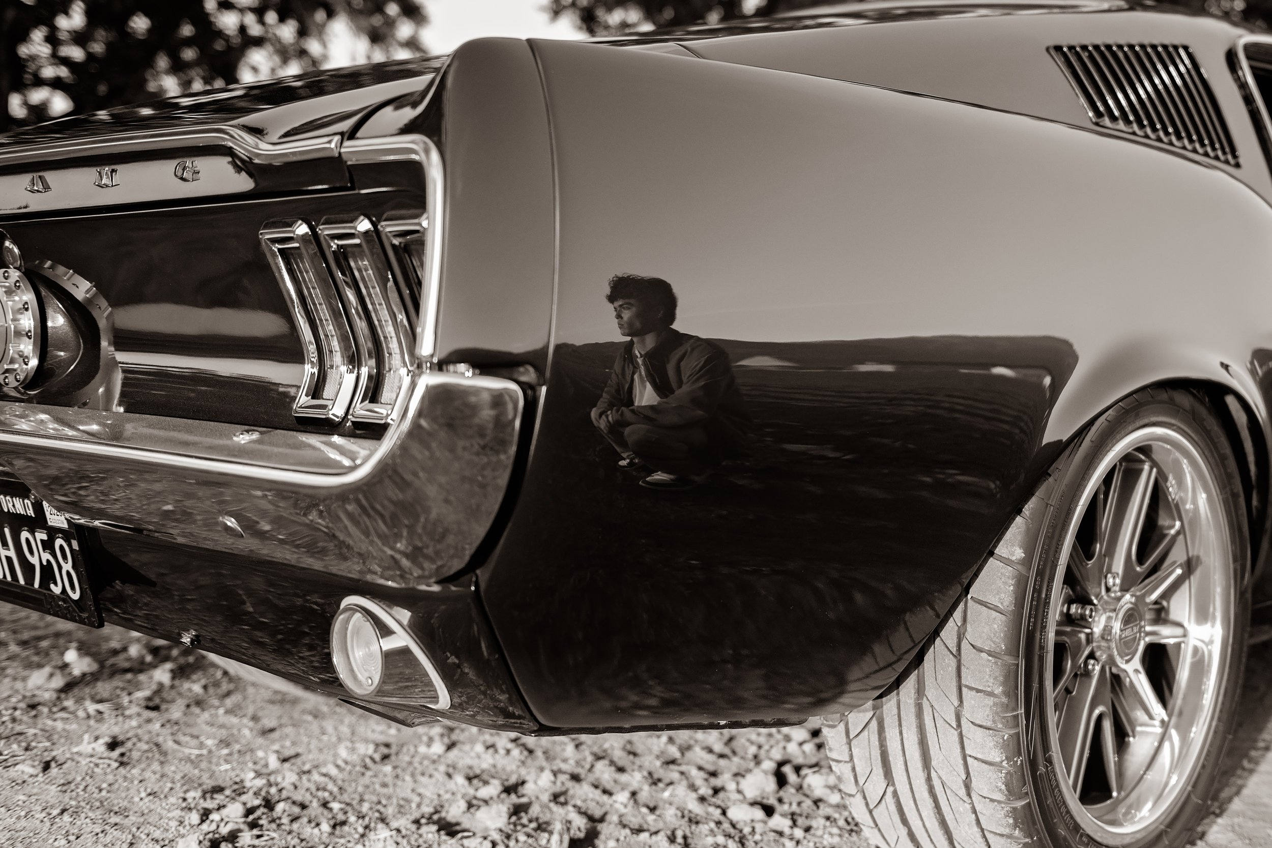 Black-and-white detail photograph showing Cruz reflected in the side of his vintage Mustang during his senior session.