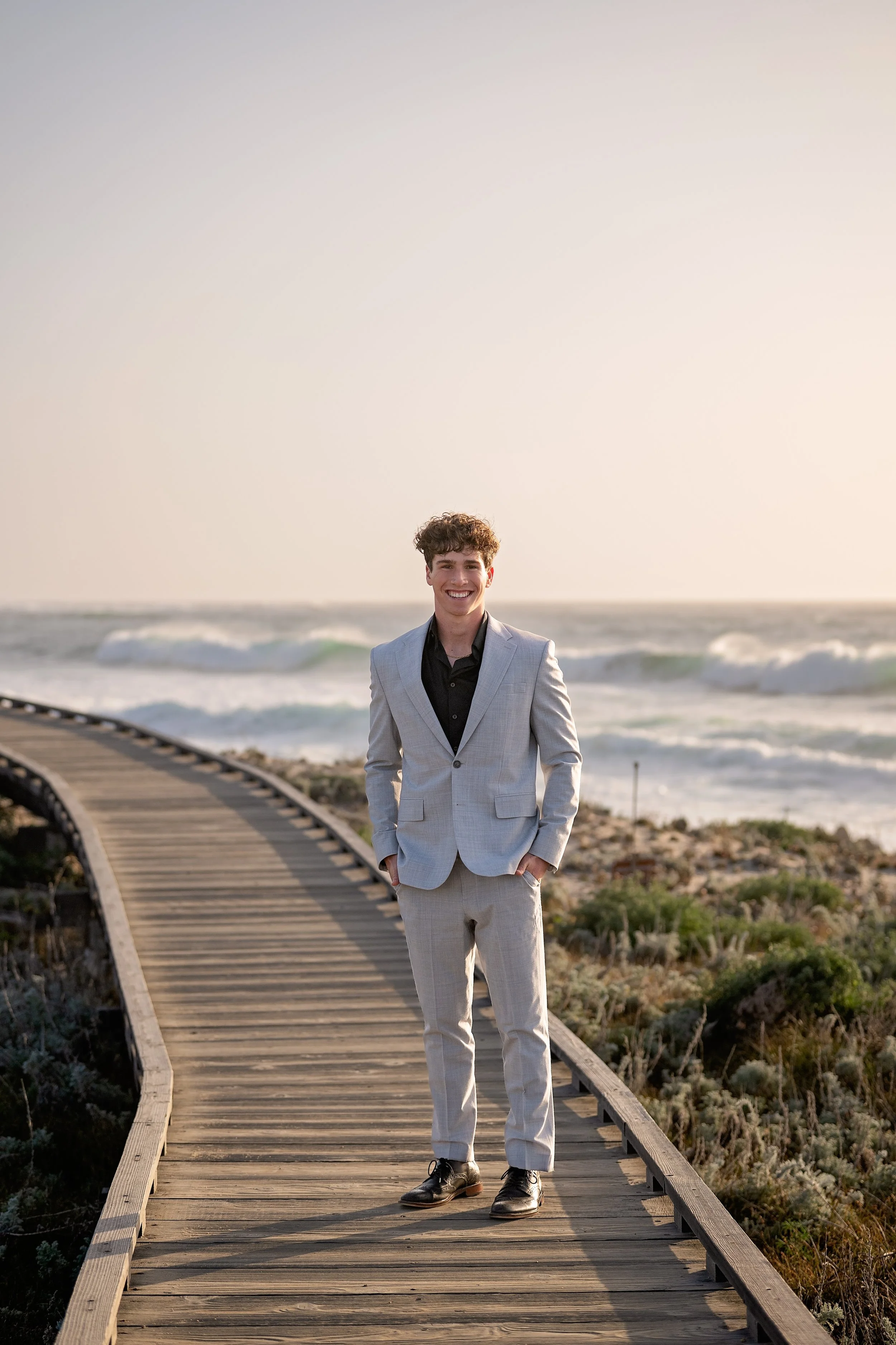 Grant Senior picture wearing a suit and standing on the beach boardwalk in Monterey