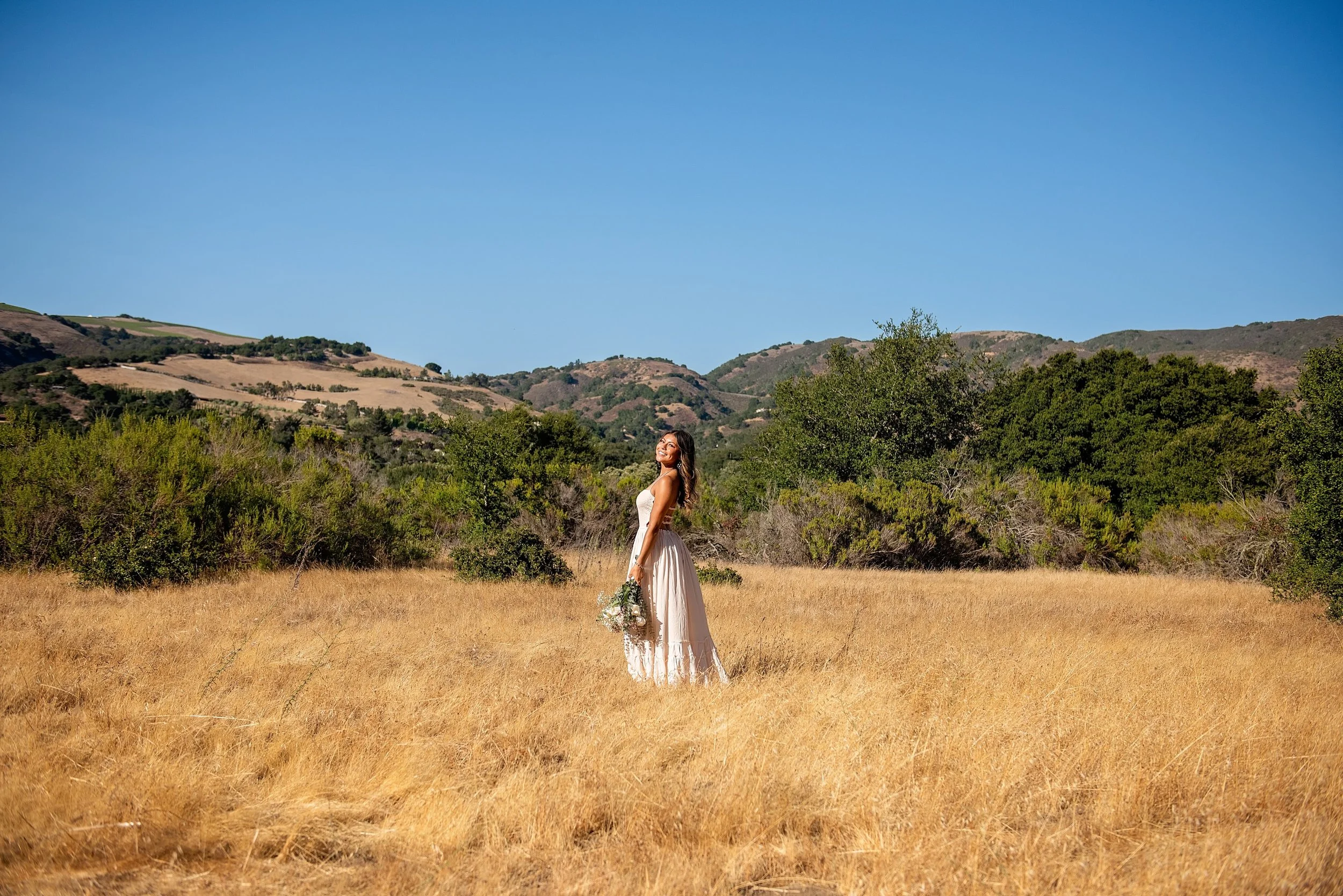Wide senior portrait of Aubrey standing in a golden field surrounded by Carmel Valley hills at Garland Ranch