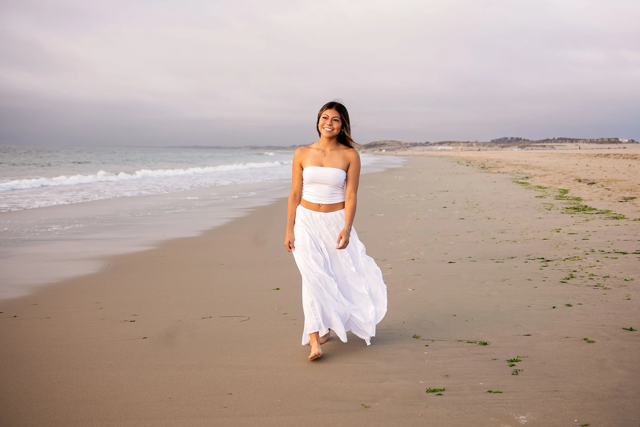 Aubrey walking barefoot along Del Monte Beach in Monterey during her senior portrait session