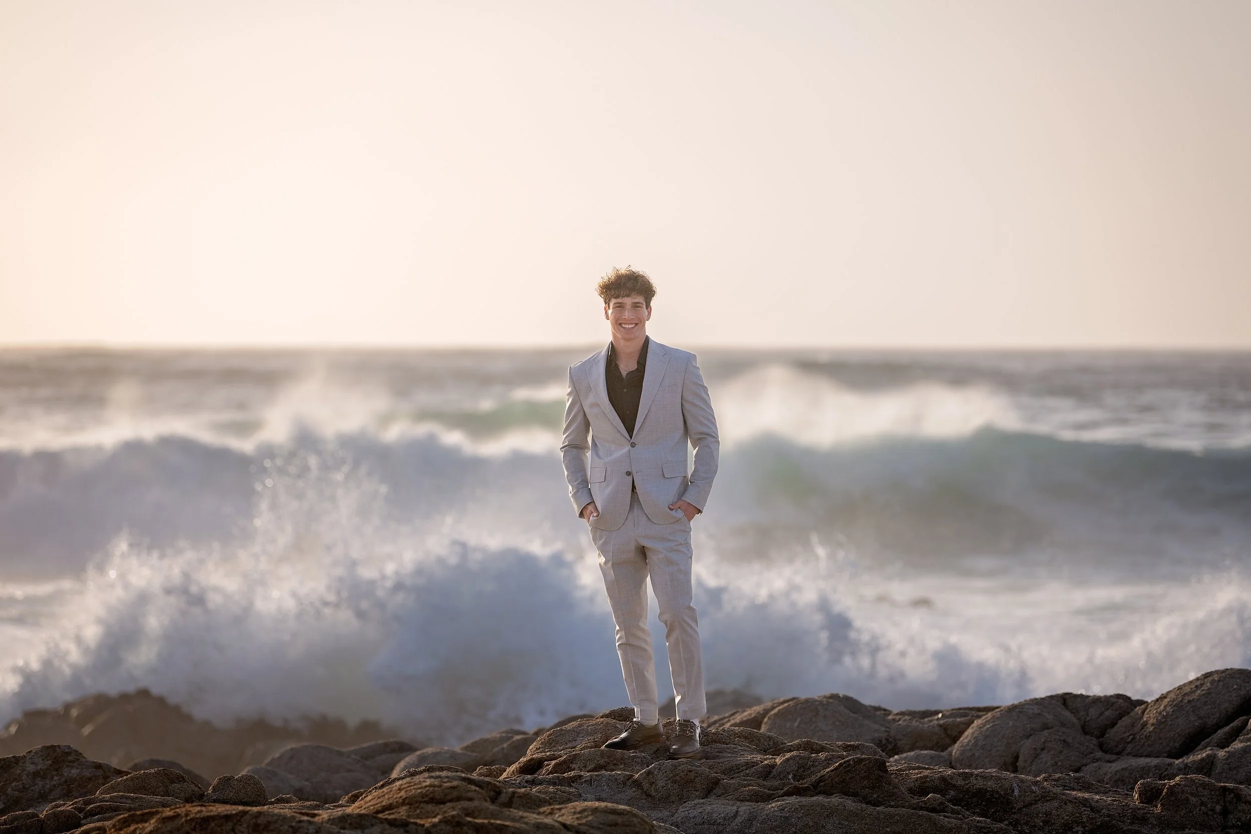Grant in a gray suit standing on cliffs above the crashign waves