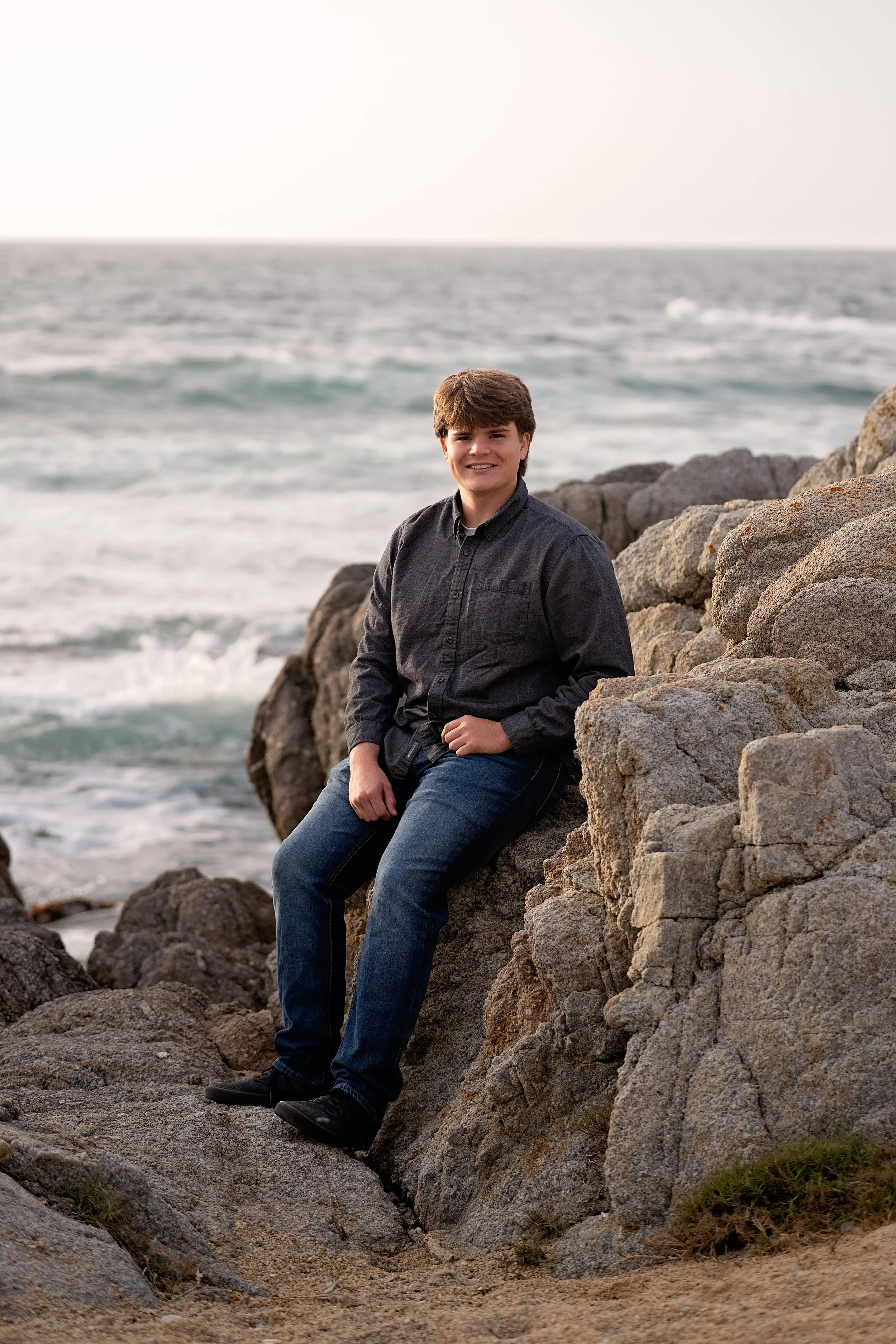 Gianni sitting among coastal rocks with the Pacific Ocean behind him at Asilomar State Beach.