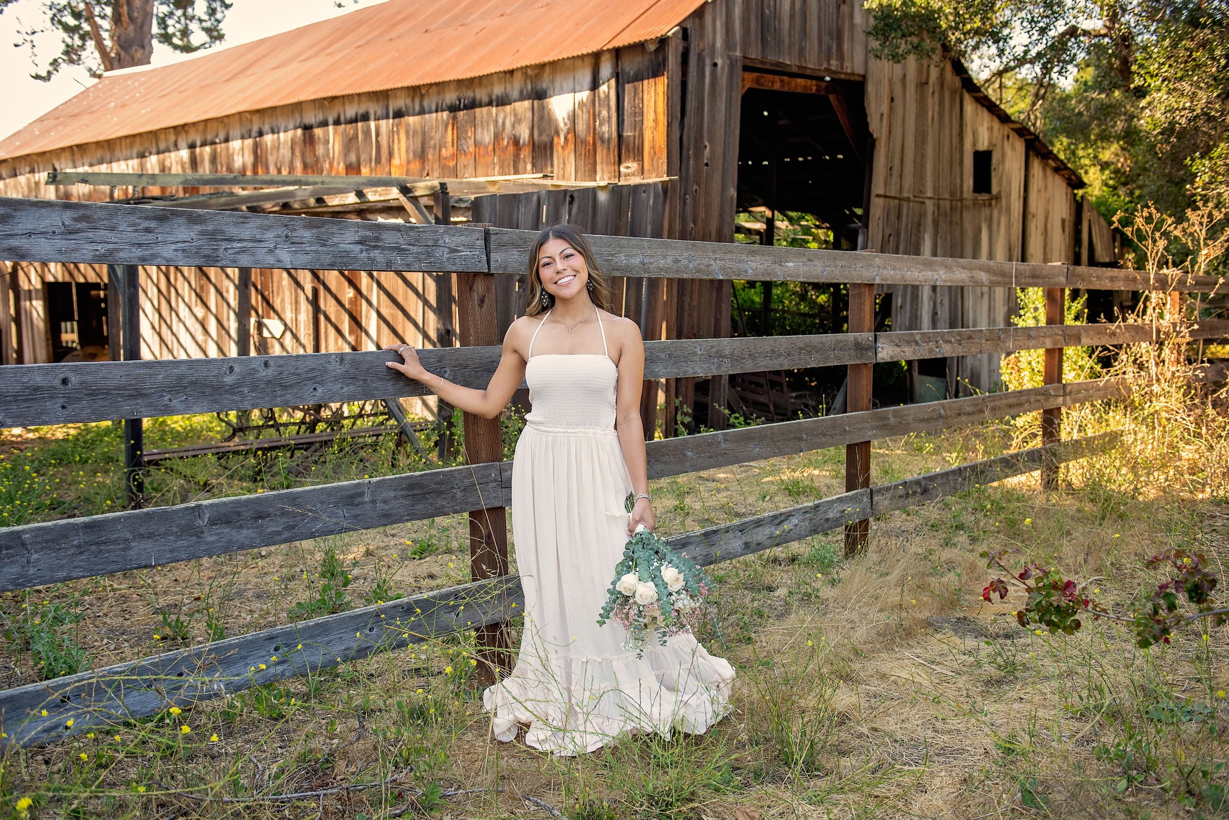 Aubrey posing in a white dress in front of a rustic barn at Garland Ranch during her senior portrait session